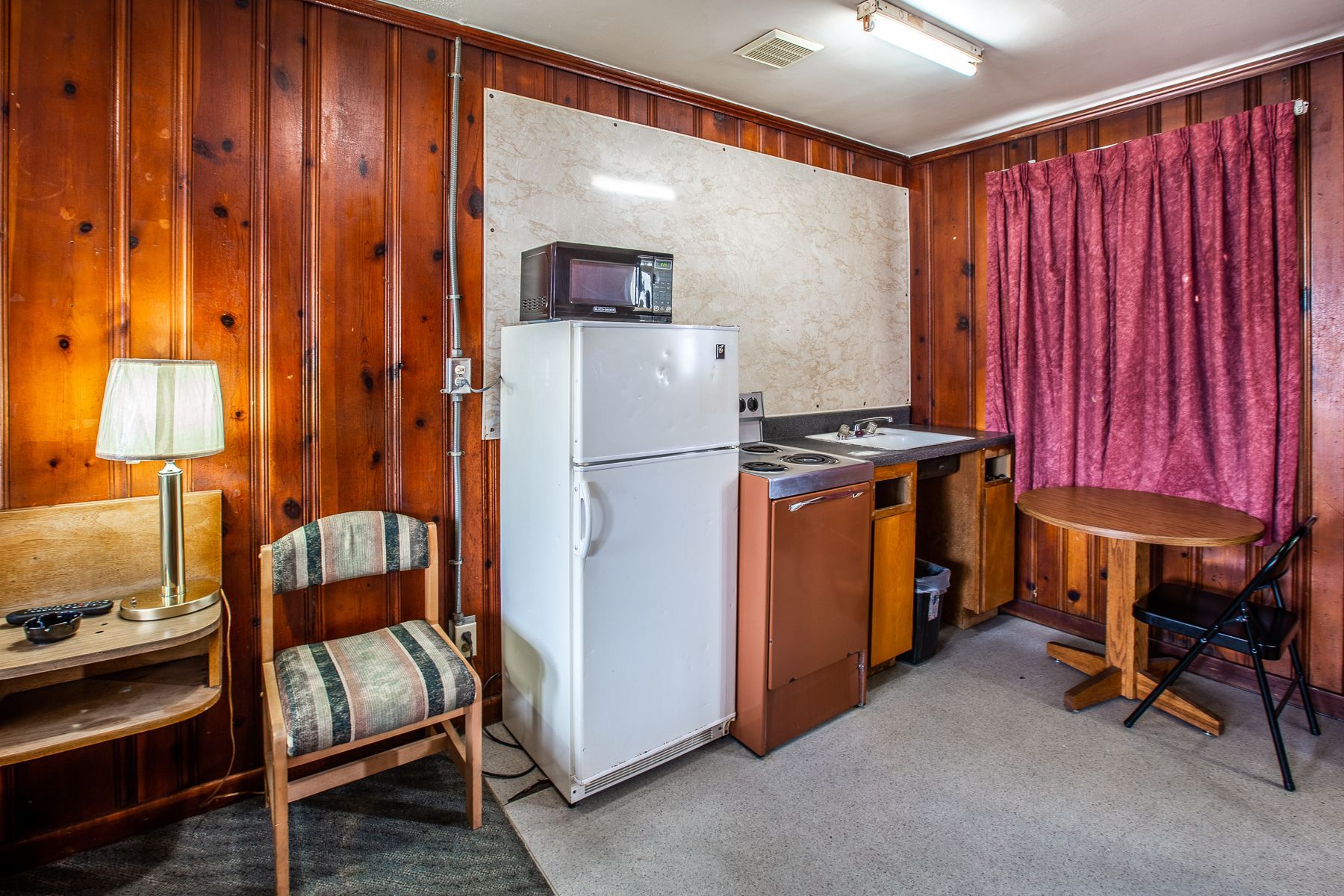 A hotel room with a refrigerator , microwave , table and chairs.