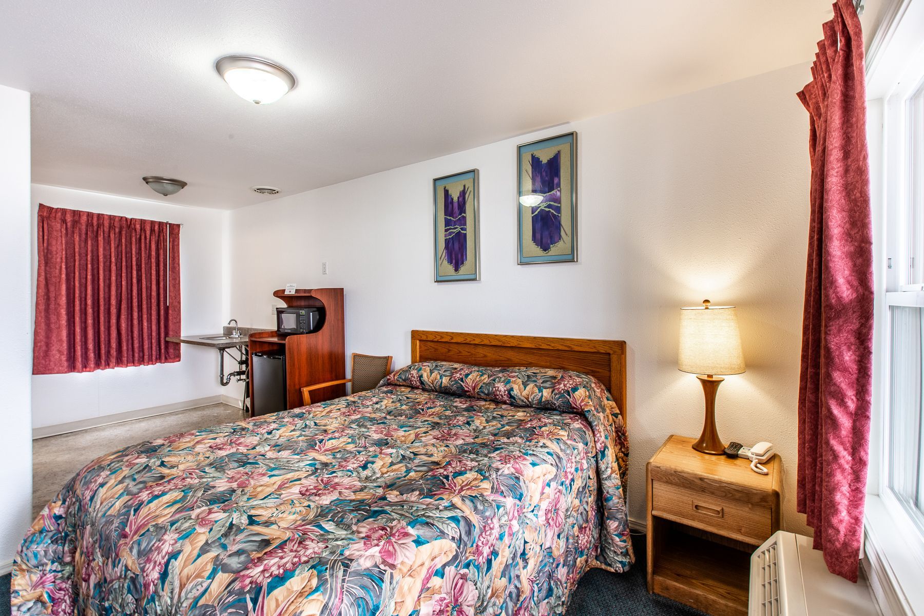 A hotel room with a bed , nightstand , lamp and window.