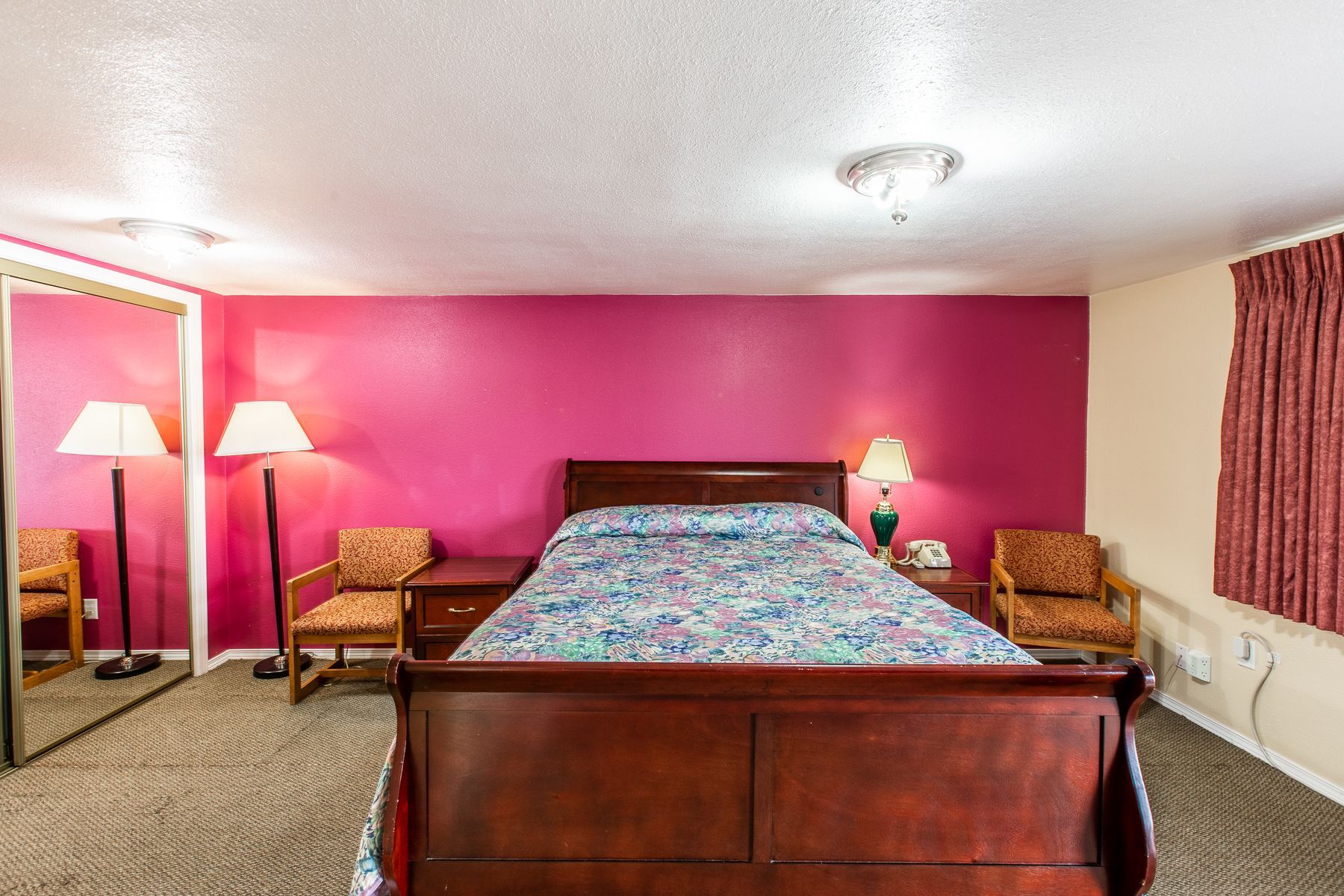 A hotel room with a bed , chairs , lamps and a mirror.