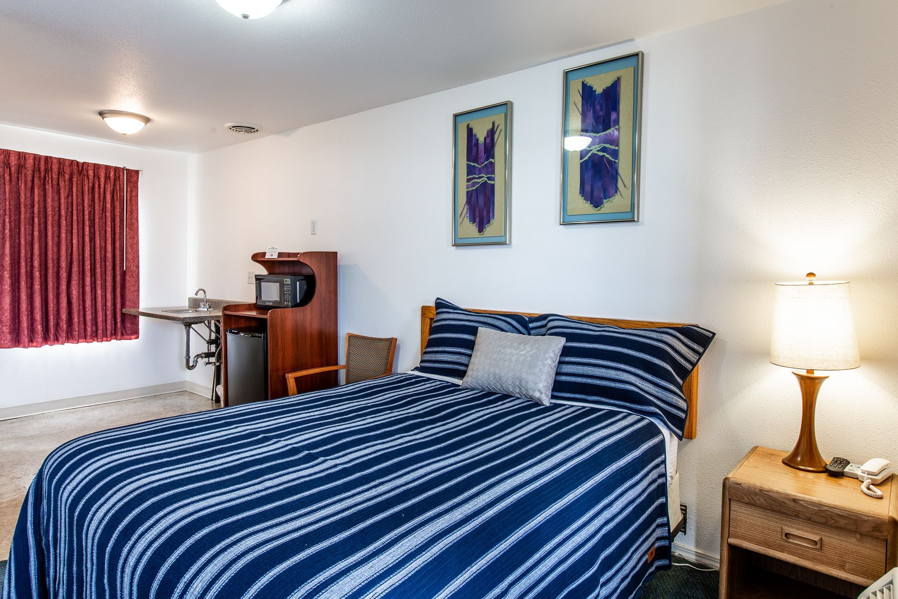 A hotel room with a bed , nightstand , lamp and microwave.