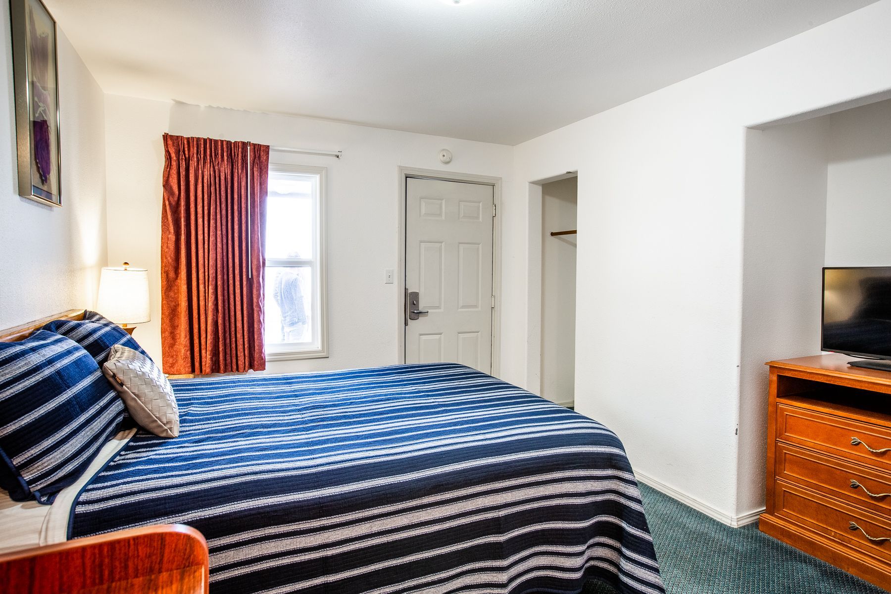 A hotel room with a bed , dresser , and television.