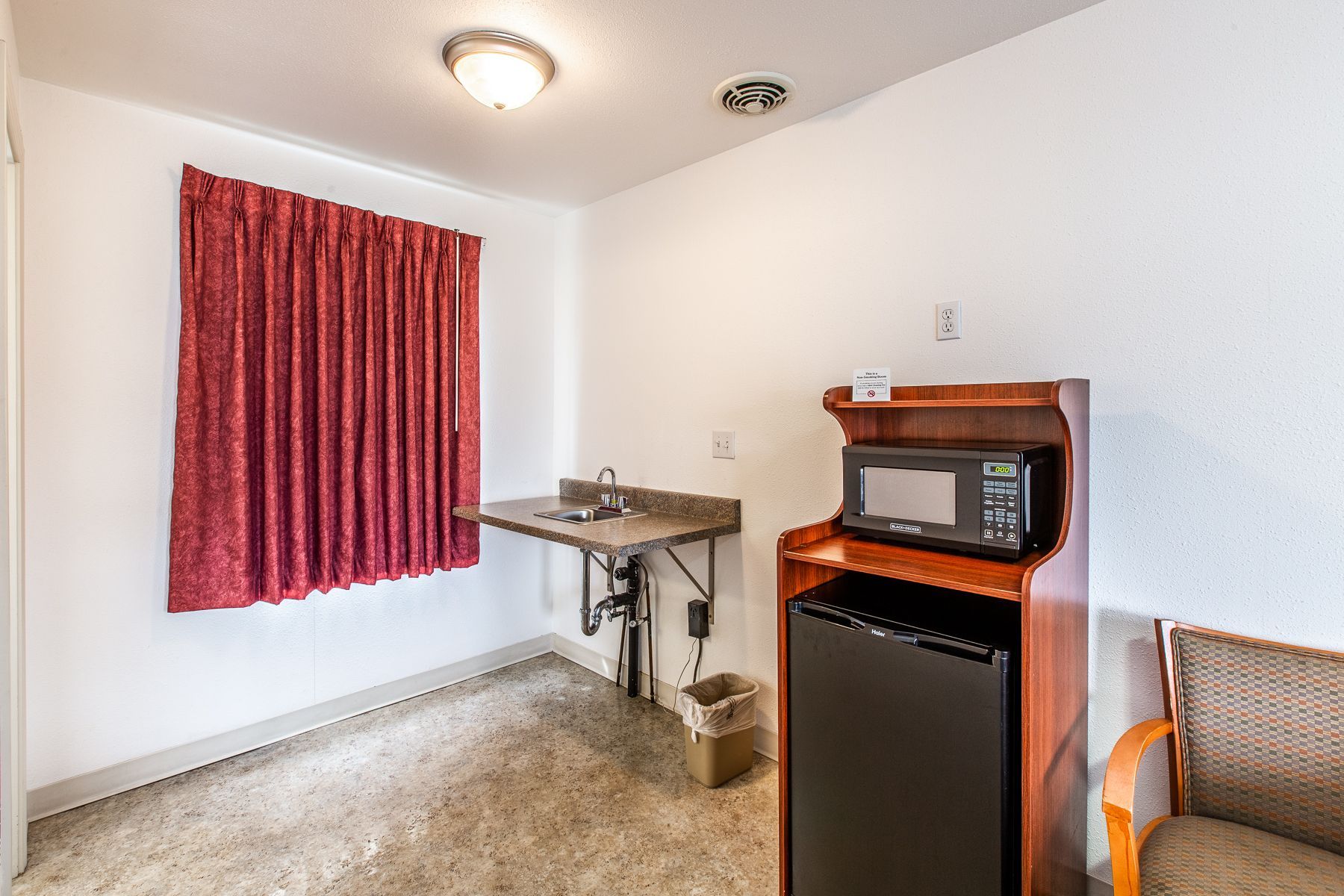 A hotel room with a microwave , refrigerator , sink and chair.