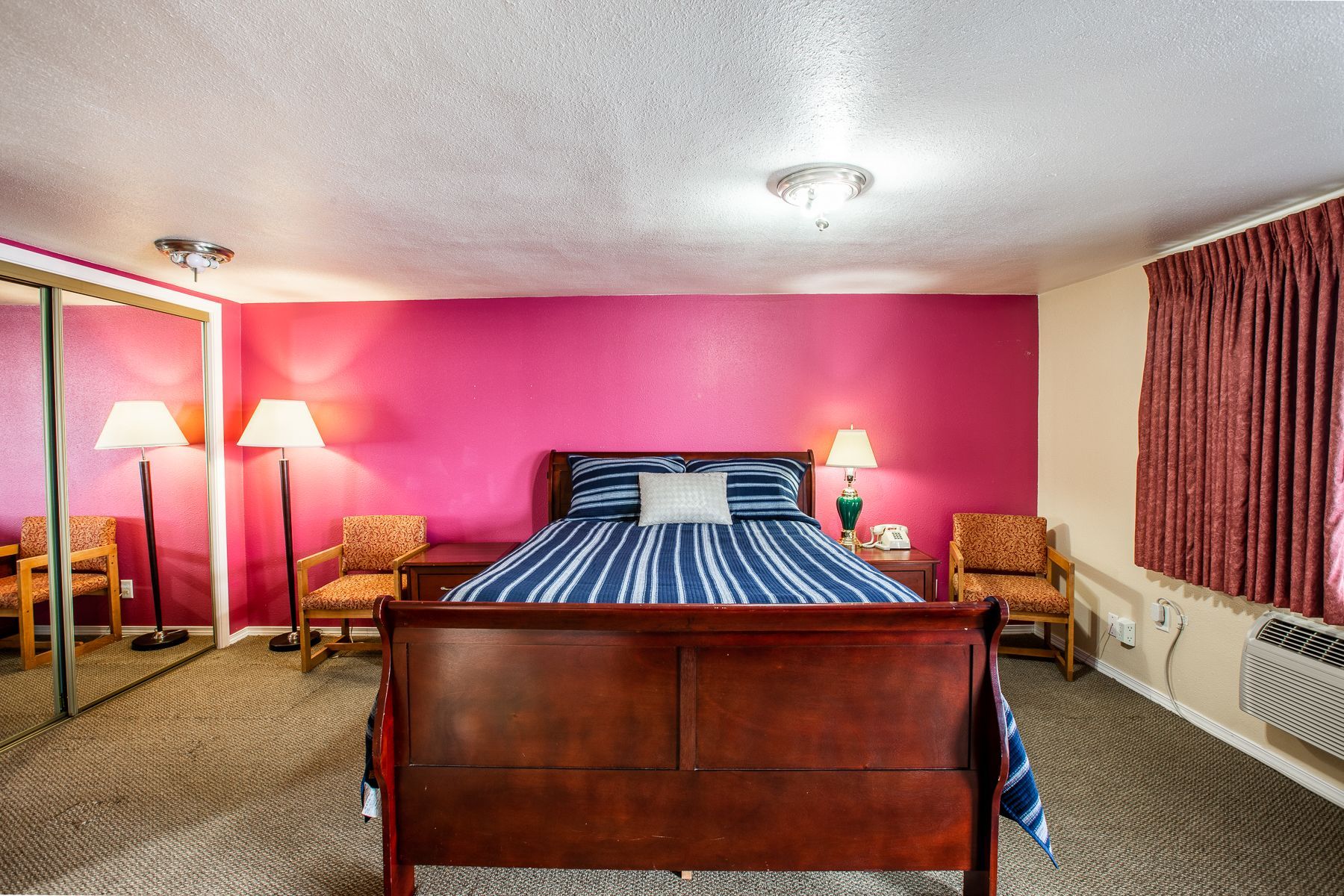 A hotel room with a king size bed , chairs , lamps and a mirror.
