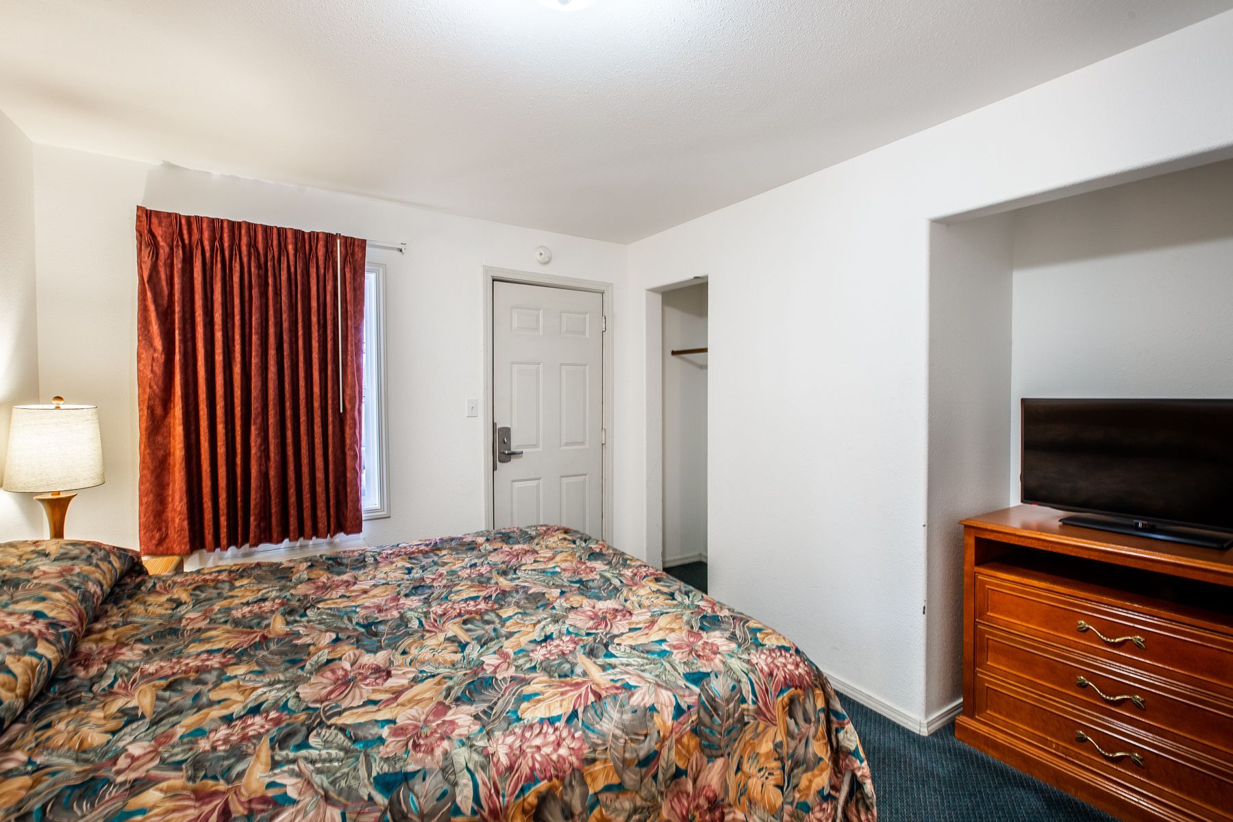A hotel room with a bed , television and dresser.
