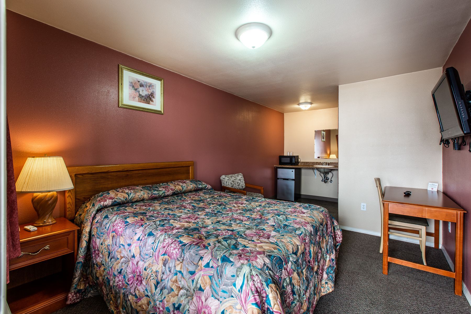 A hotel room with a bed , desk , lamp and television.