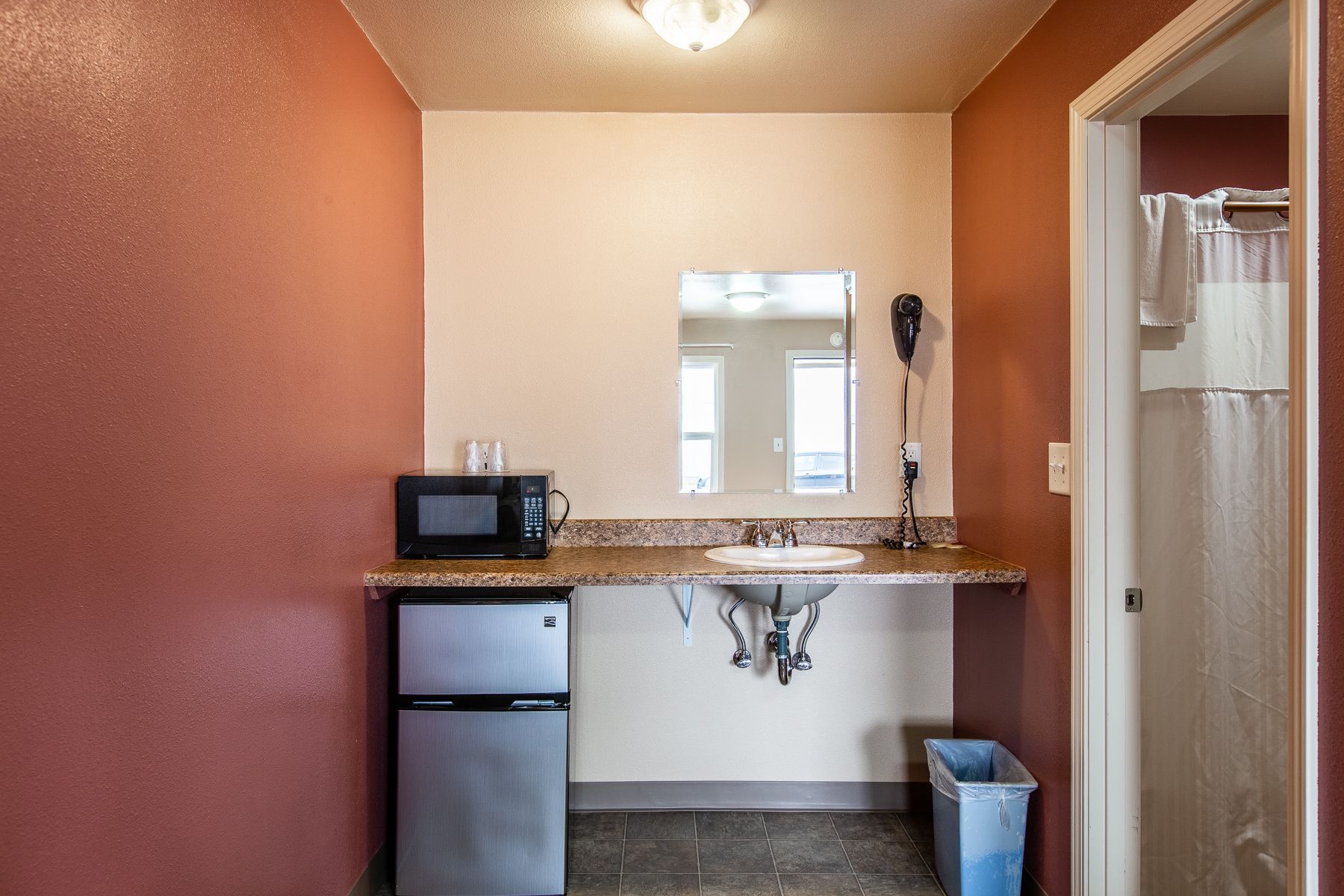 A bathroom with a sink , refrigerator , microwave and mirror.