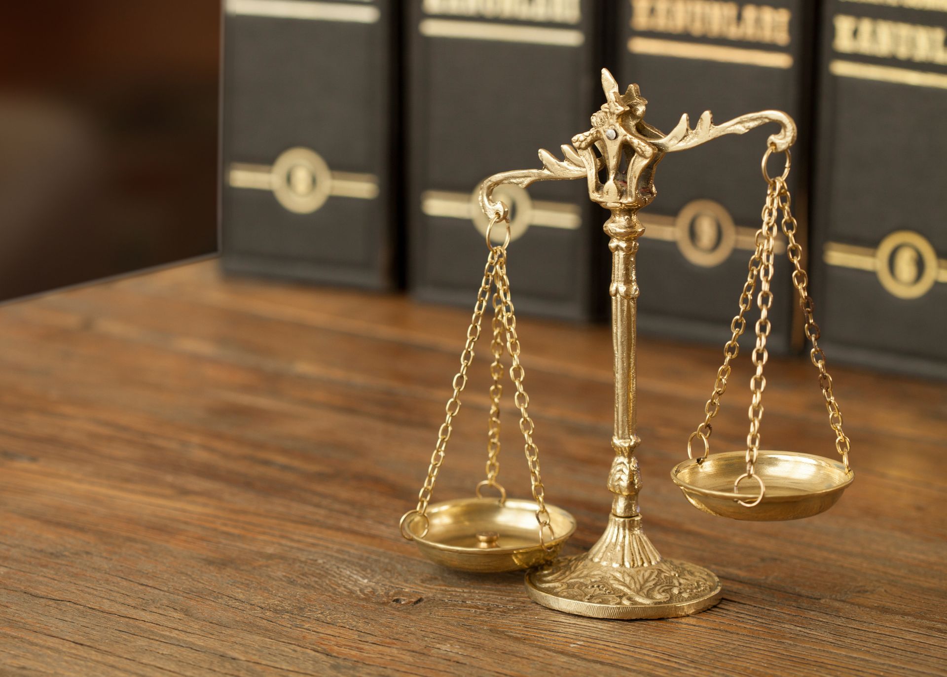 Golden scales of justice on wooden table, with blurry black files, representing criminal lawyers.