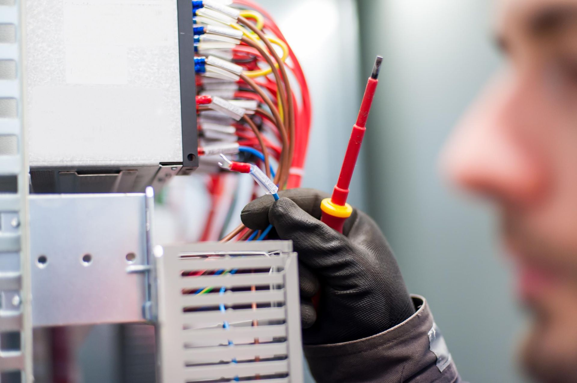 A Man Is Holding A Screwdriver In Front Of A Bunch Of Wires — Connect Mid Coast Electrical Services In Taree, NSW