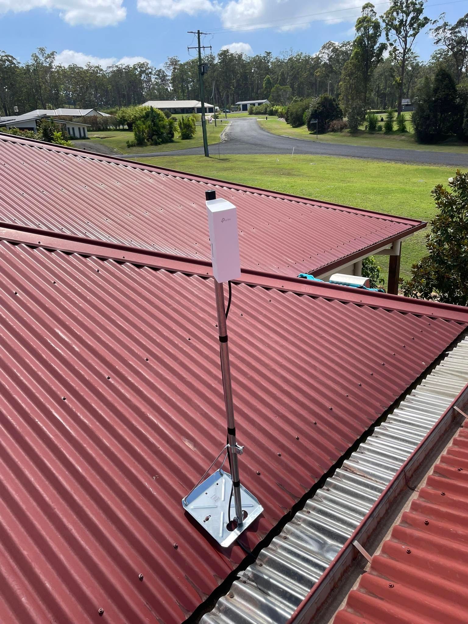 White antenna mounted on a red corrugated metal roof with a grassy yard and trees beyond — Connect Mid Coast Electrical Services In Taree, NSW