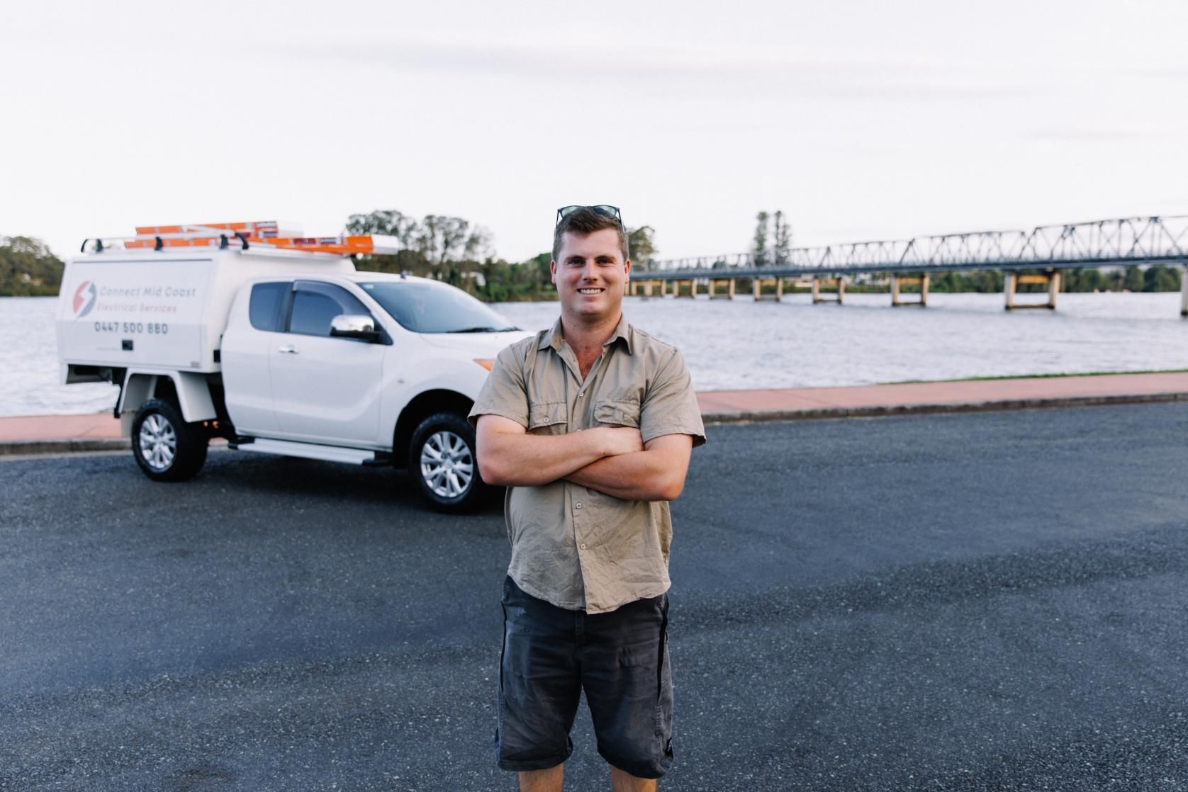 A Man Is Standing In Front Of A White Truck With His Arms Crossed — Connect Mid Coast Electrical Services In Taree, NSW