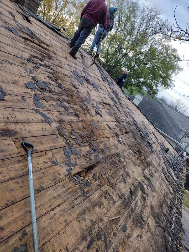 Three people work on a sloped roof with exposed wooden boards after removing shingles.
