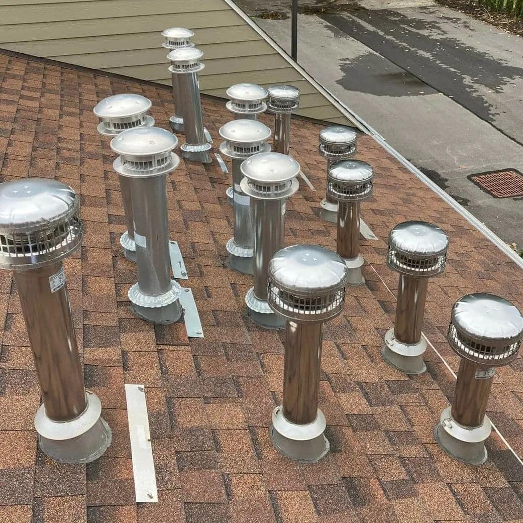 A shingled residential roof with multiple metal vent pipes of varying heights topped with protective covers.