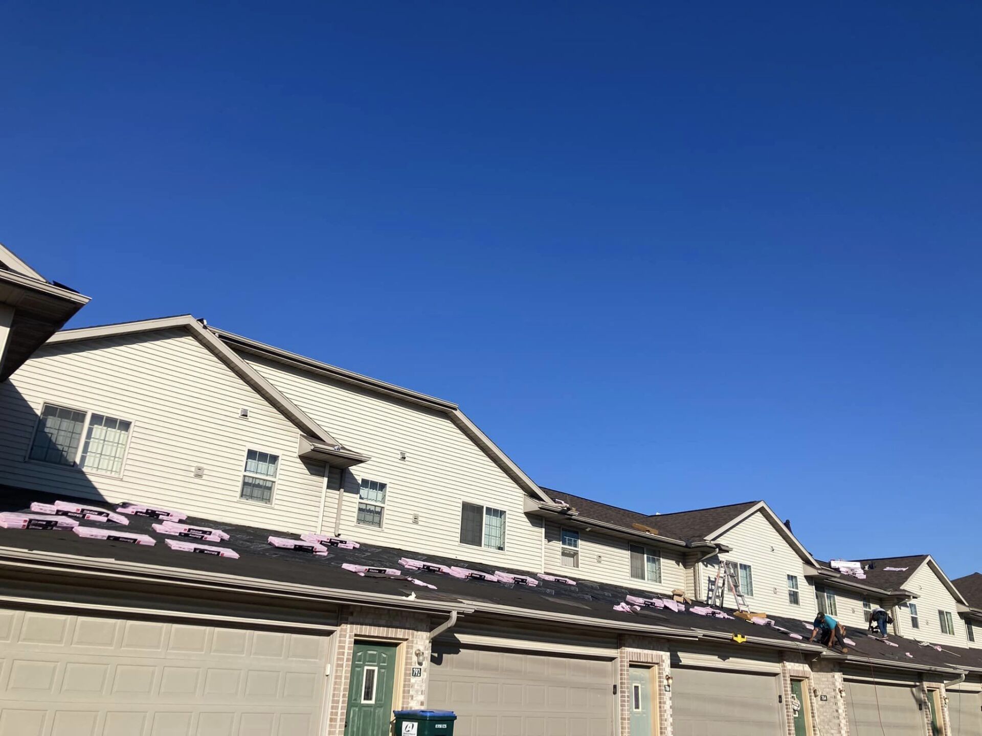 A tan multi-unit townhome building under a clear blue sky, featuring a roof covered with pink building materials.