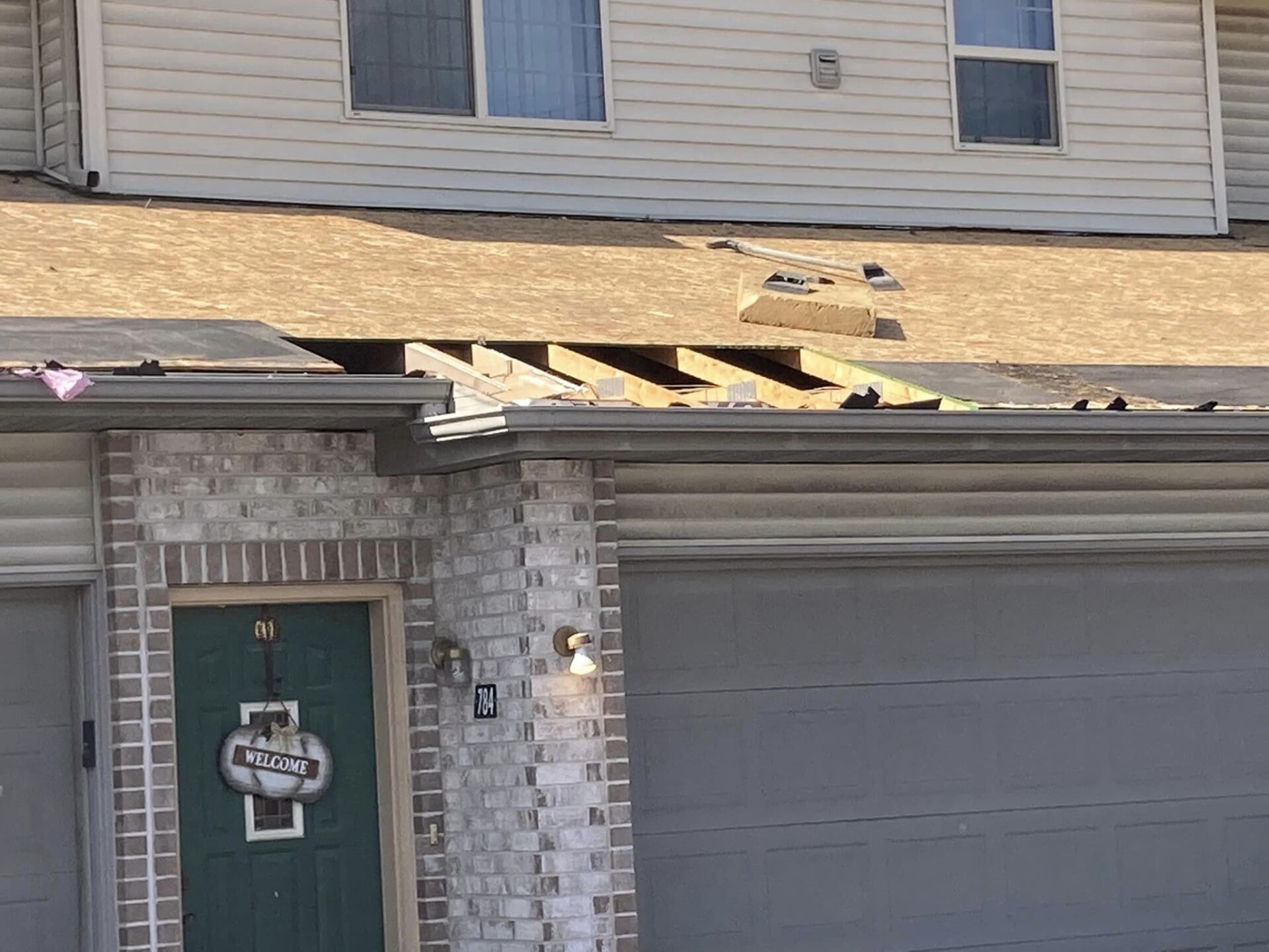 A residential house with damaged roofing where a section of shingles and decking is missing, exposing the wooden rafters.