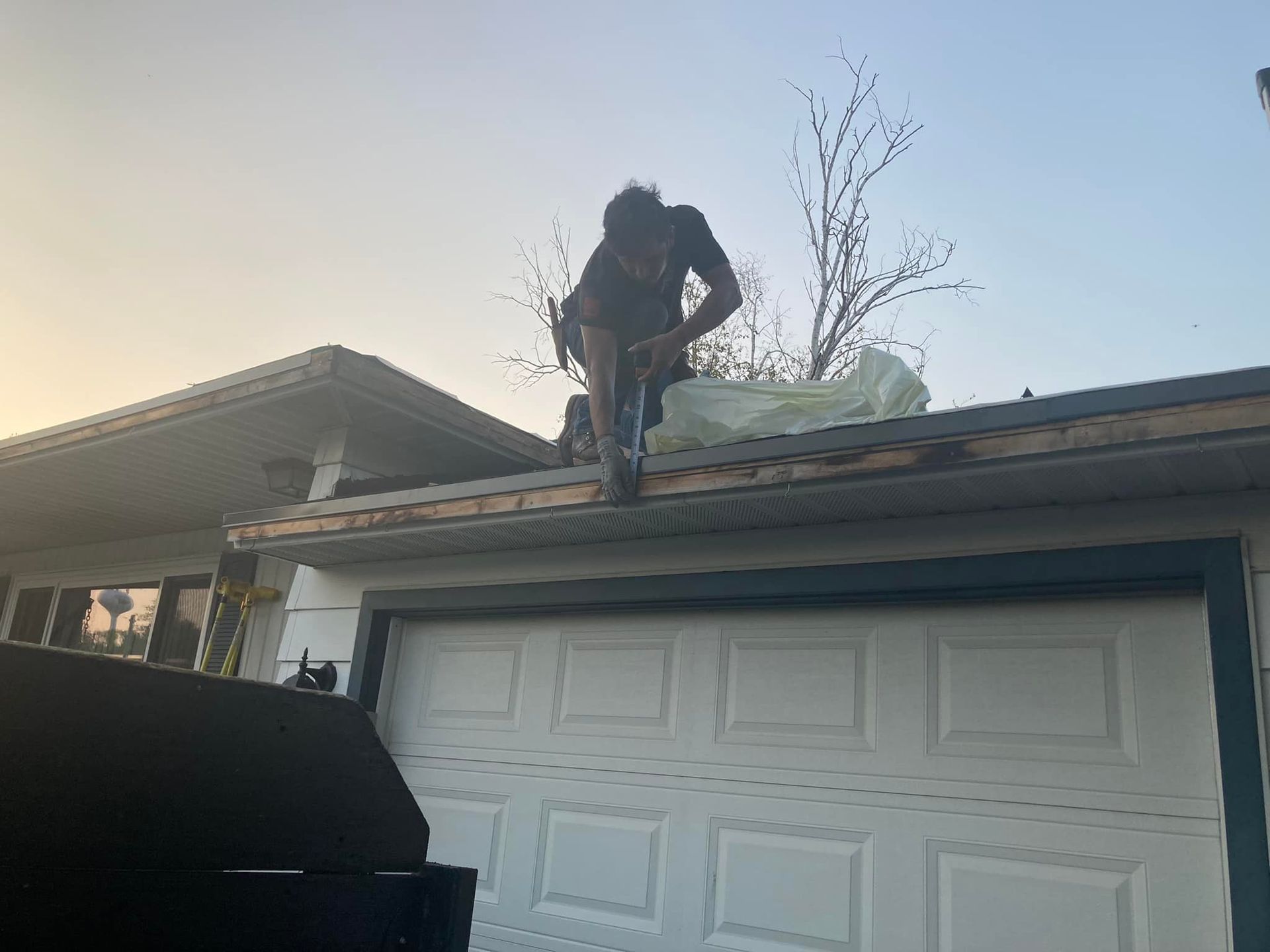 A person stands on the roof of a garage above a white door, working on the fascia board or gutter area.