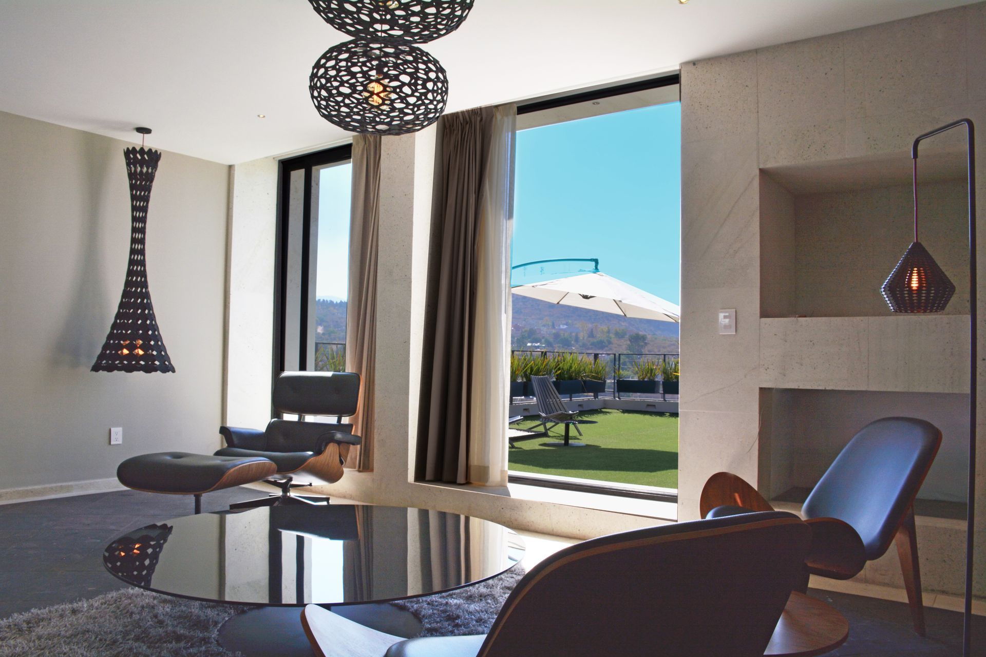 Moderna sala de estar con muebles oscuros, grandes ventanales y vista al exterior.
