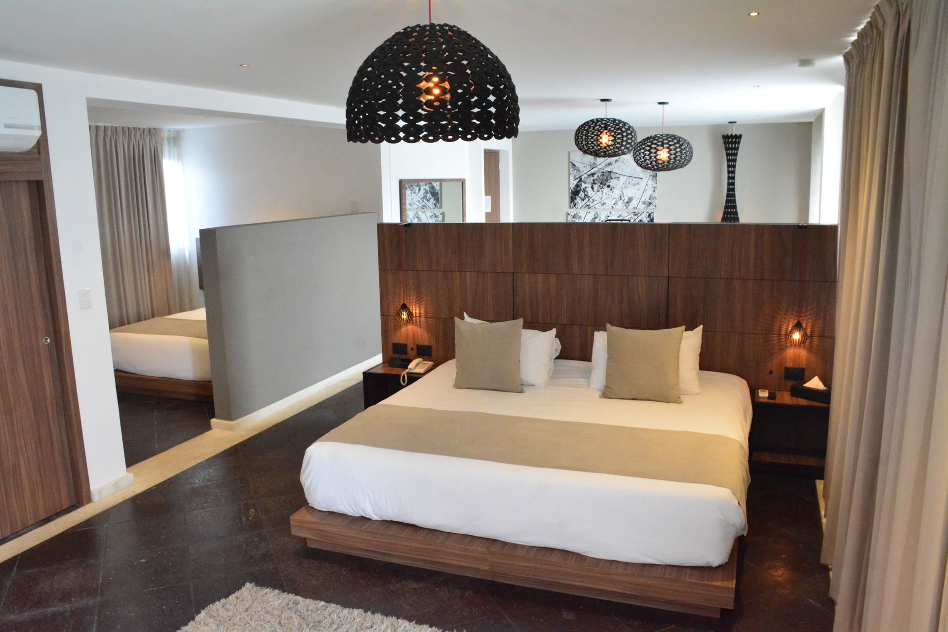 Moderna suite de hotel con una cama tamaño king, detalles en madera oscura y una zona de estar separada con otra cama.