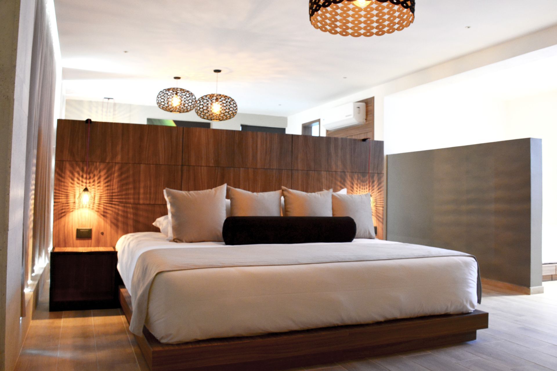 Dormitorio moderno con cama King, cabecera de madera y luces colgantes decorativas.