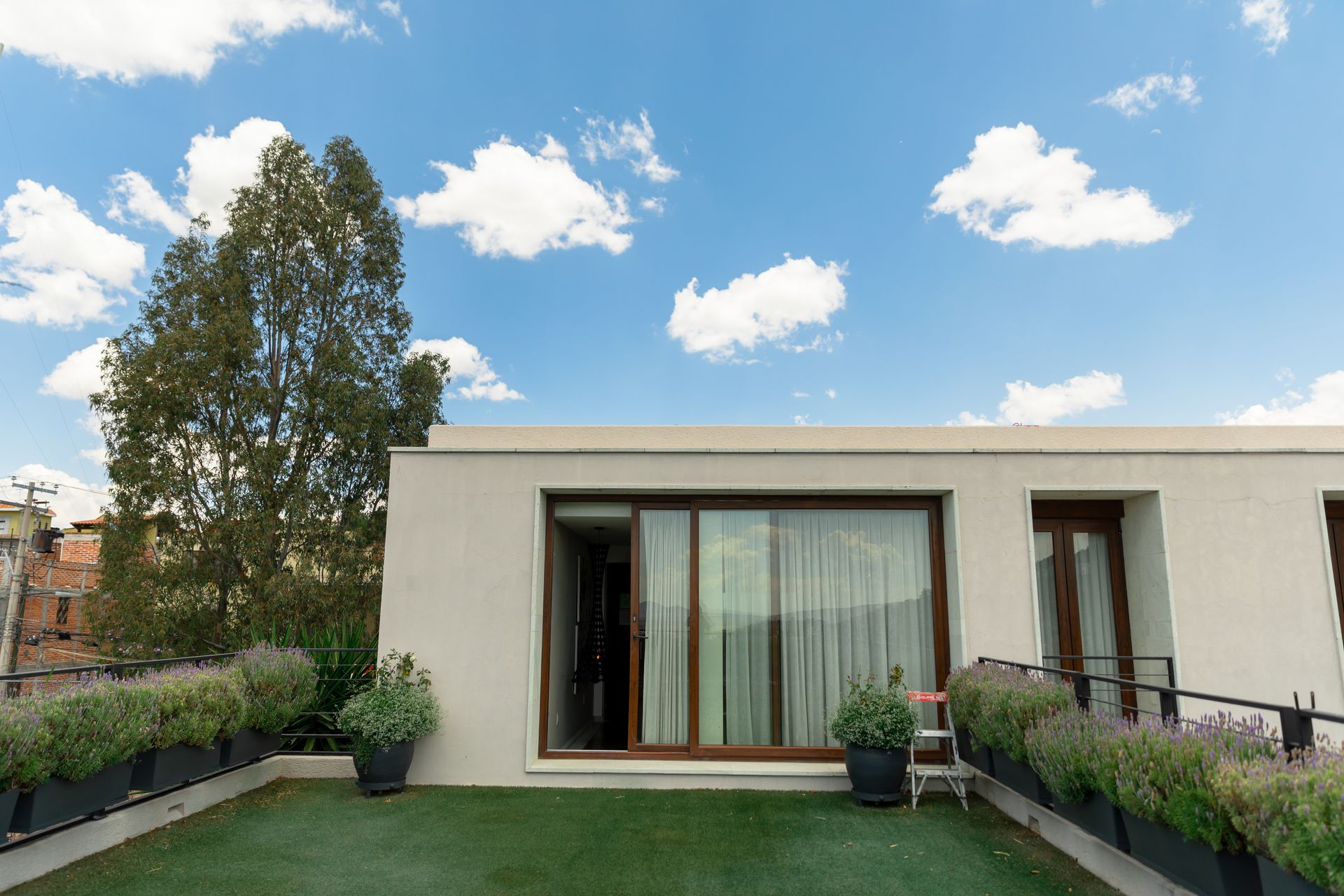 Terraza en la azotea con césped artificial, cojines de salón, plantas en macetas y puerta corrediza de vidrio