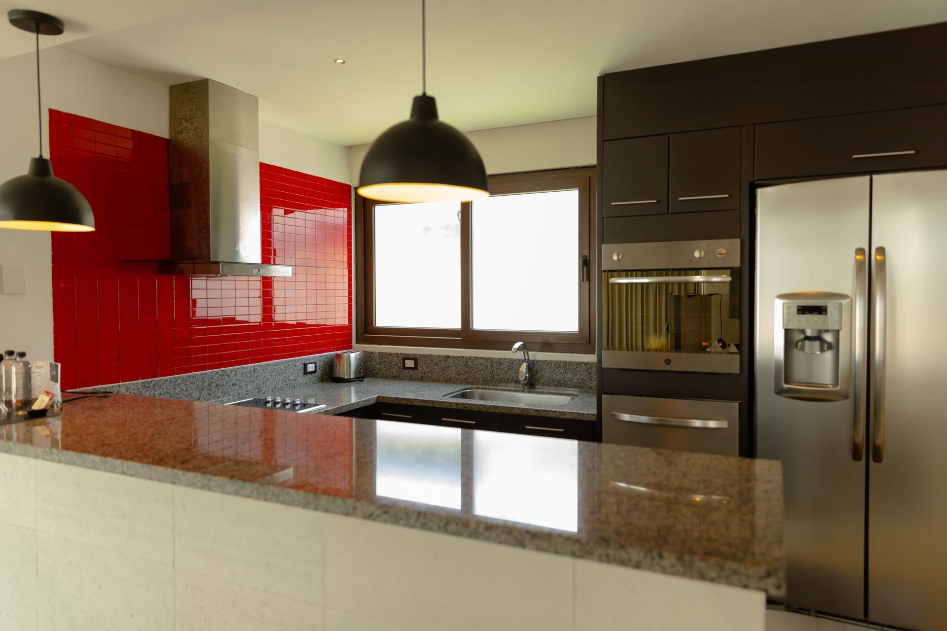 Cocina moderna con salpicadero de azulejos rojos, encimeras de granito y electrodomésticos de acero inoxidable.