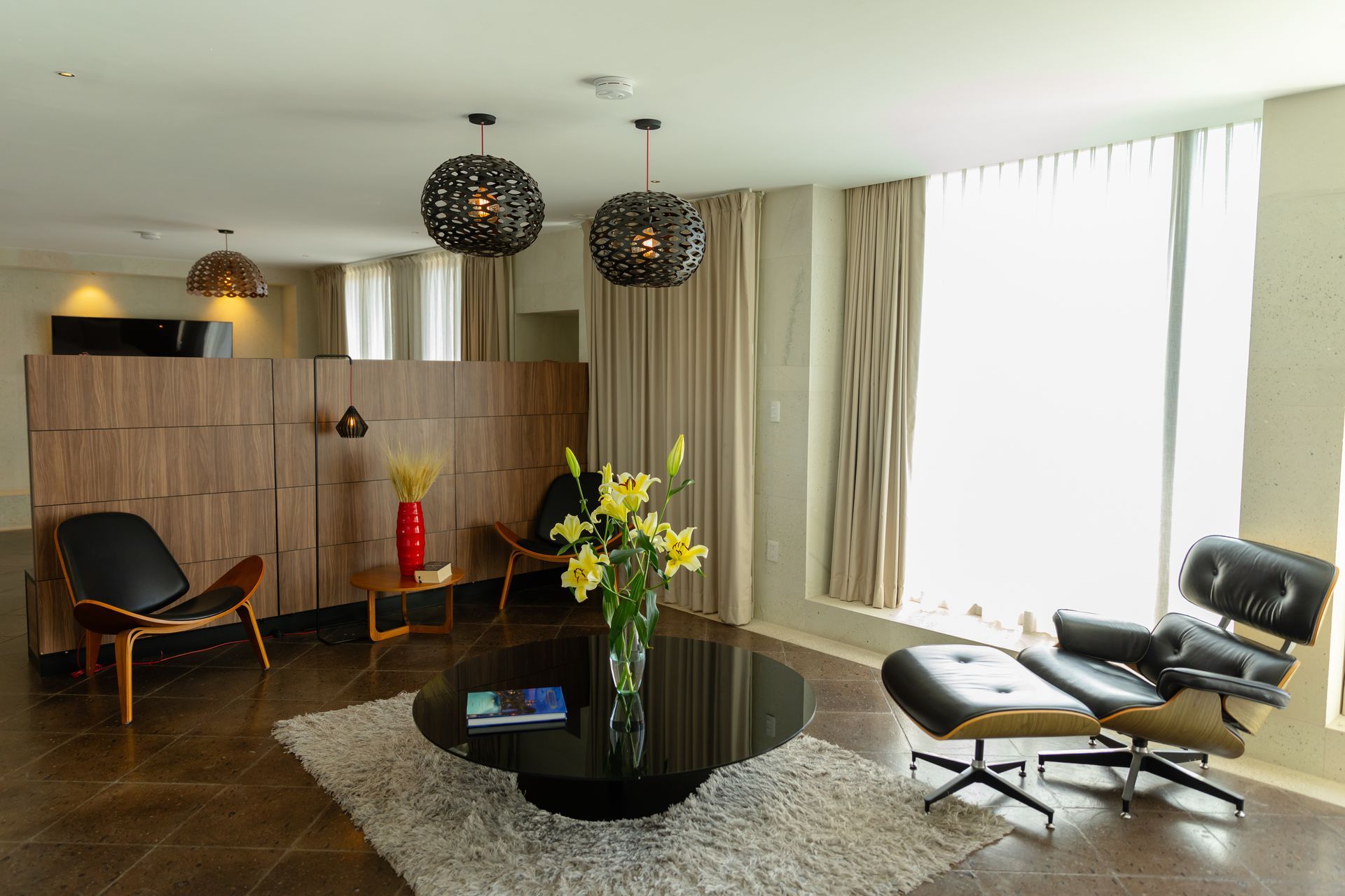 Salón moderno con sillones de cuero, madera oscura y lámparas colgantes estampadas. Una gran mesa de centro oscura.