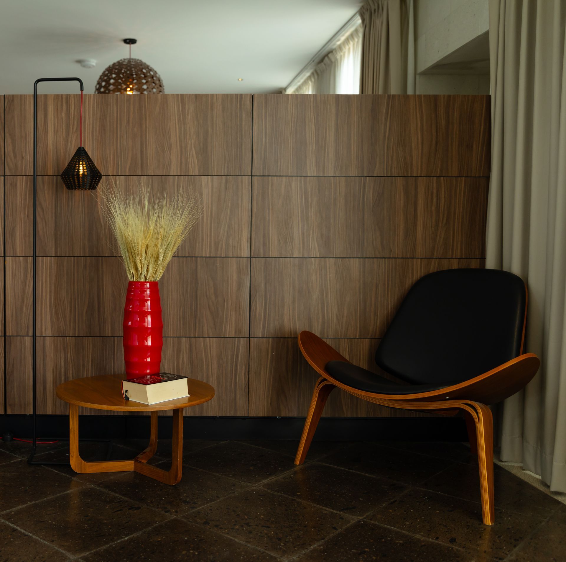Cama de hotel con cabecero de madera, mesitas de noche y lámparas colgantes; colores neutros.