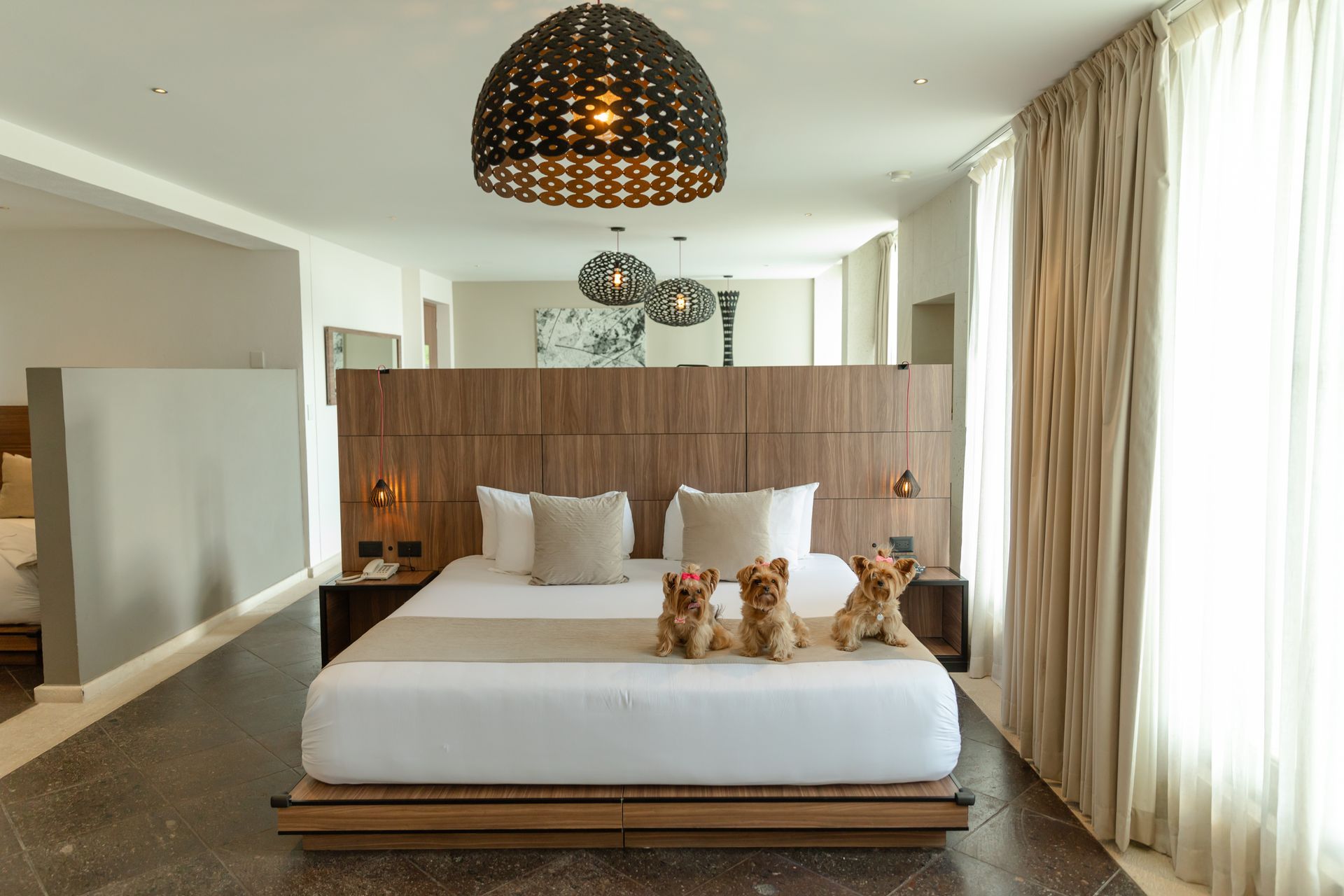 Dormitorio con cama king-size, cabecero de madera, dos lámparas colgantes y una pared parcial que separa una segunda cama.