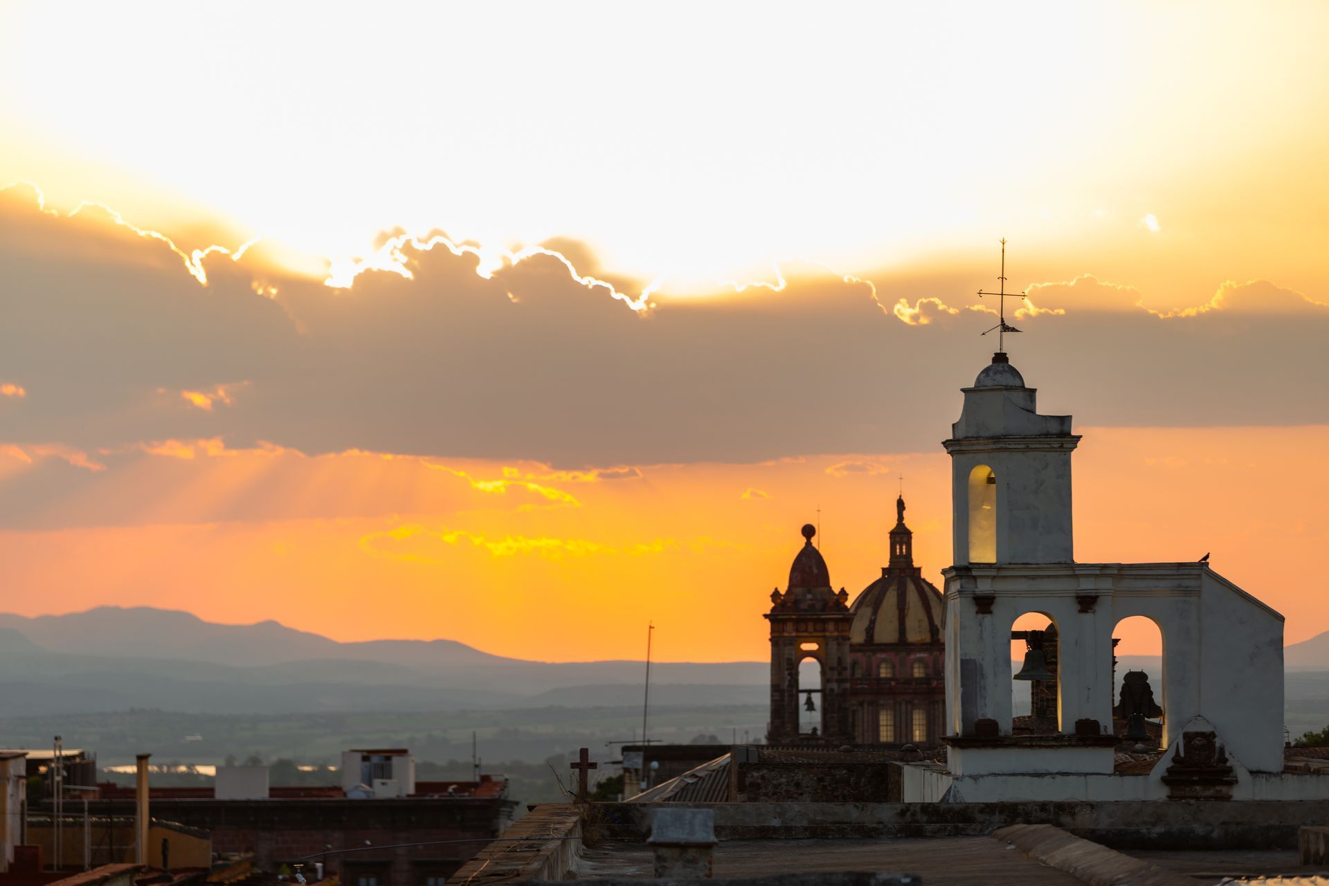 Vista de una calle de la ciudad que conduce a una iglesia rosa con torres, edificios y árboles bajo un cielo azul.