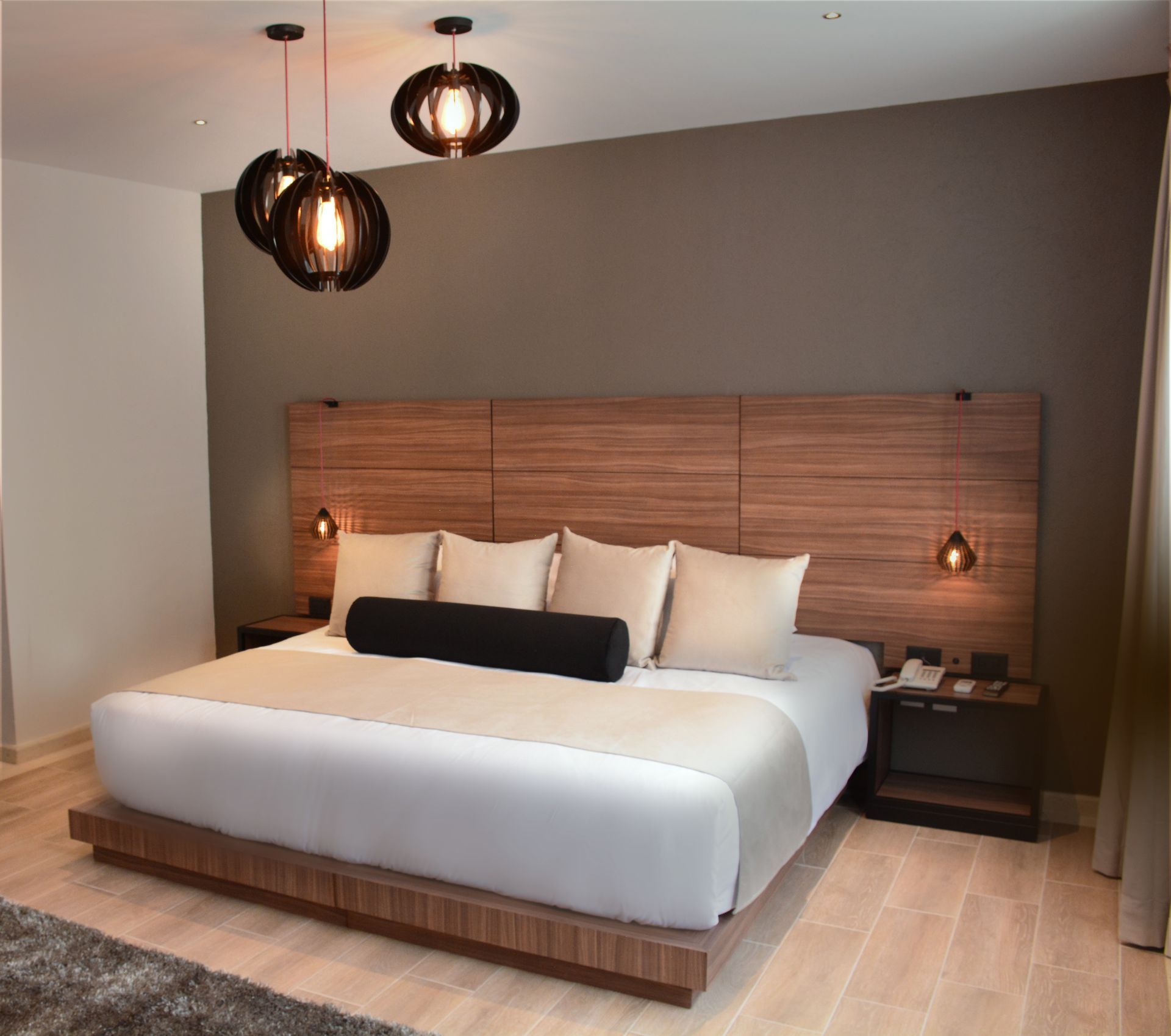 Dormitorio con cama king size, cabecero de madera, mesitas de noche y lámparas colgantes decorativas. Colores neutros.
