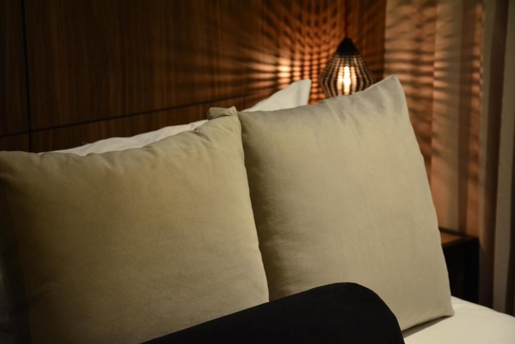 Dos almohadas cuadradas de color beige sobre una cama, iluminadas por una lámpara