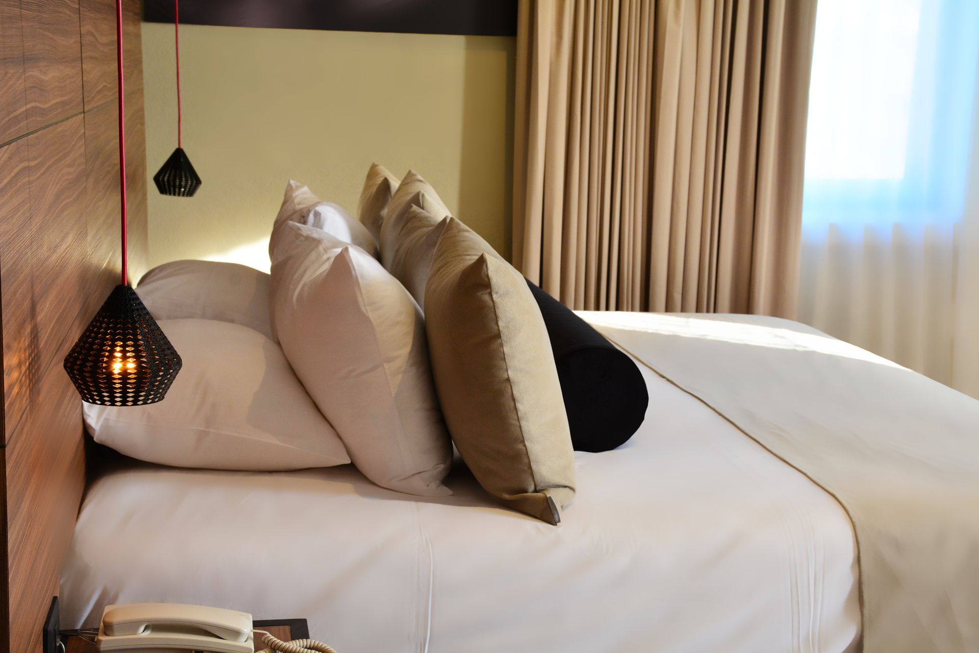 Cama con almohadas en una habitación de hotel, con luces colgantes decorativas y un teléfono de noche.