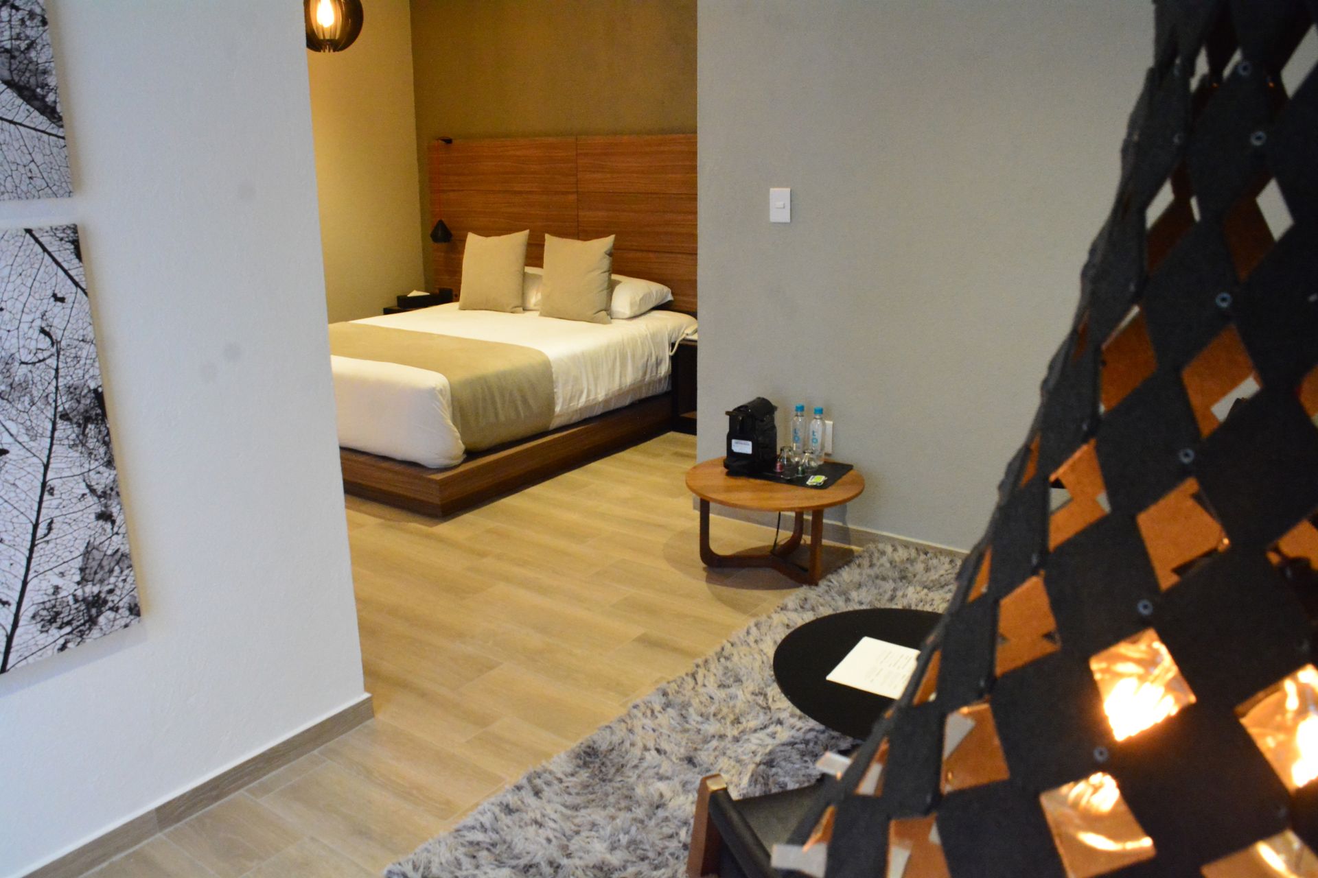Interior de habitación de hotel con una cama, una pequeña mesa redonda y una lámpara decorativa.