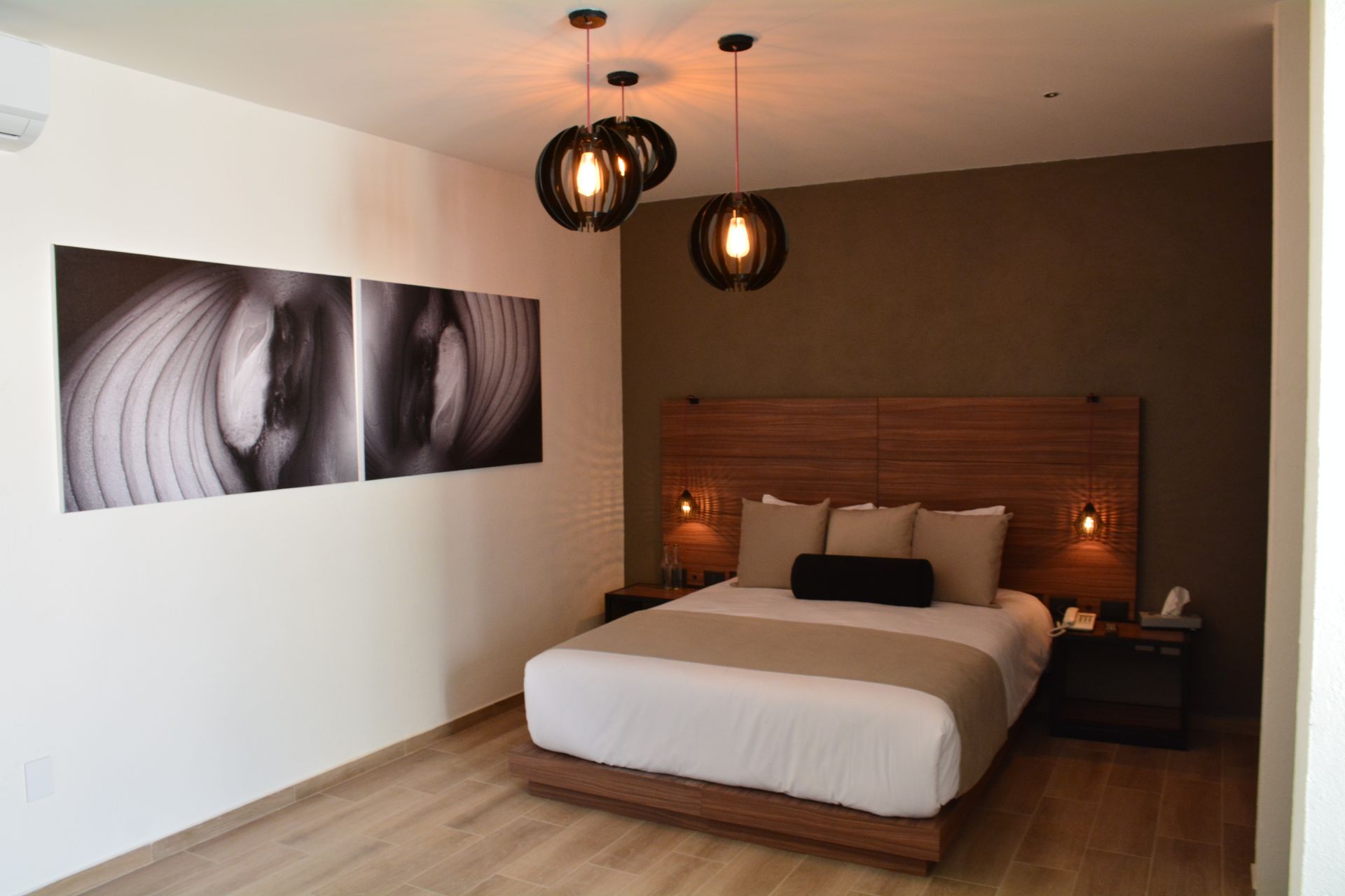 Dormitorio con pared con acento marrón, cama, obras de arte y lámparas colgantes.