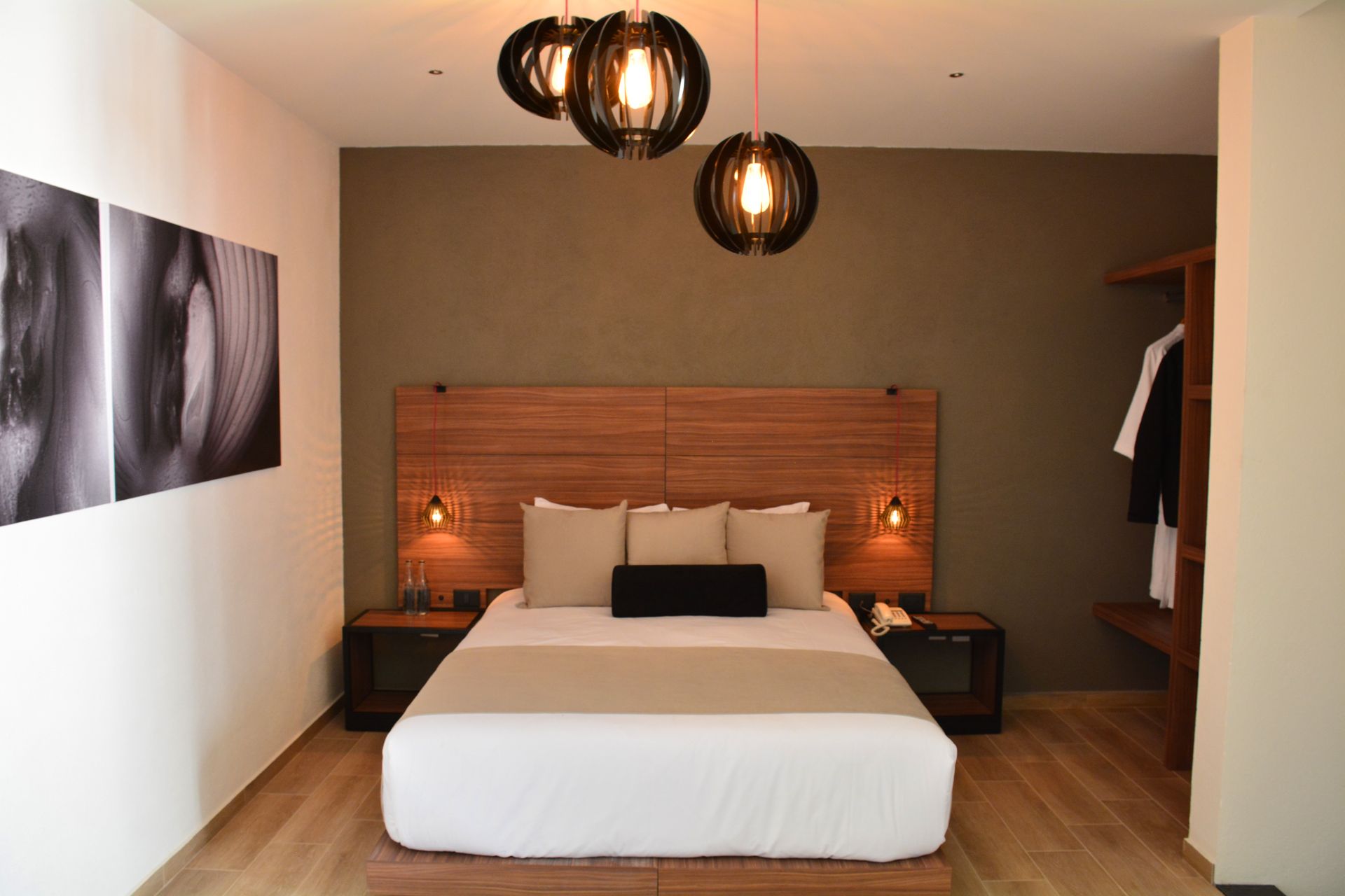 Dormitorio de hotel moderno con cama, mesitas de noche, arte y lámparas colgantes.