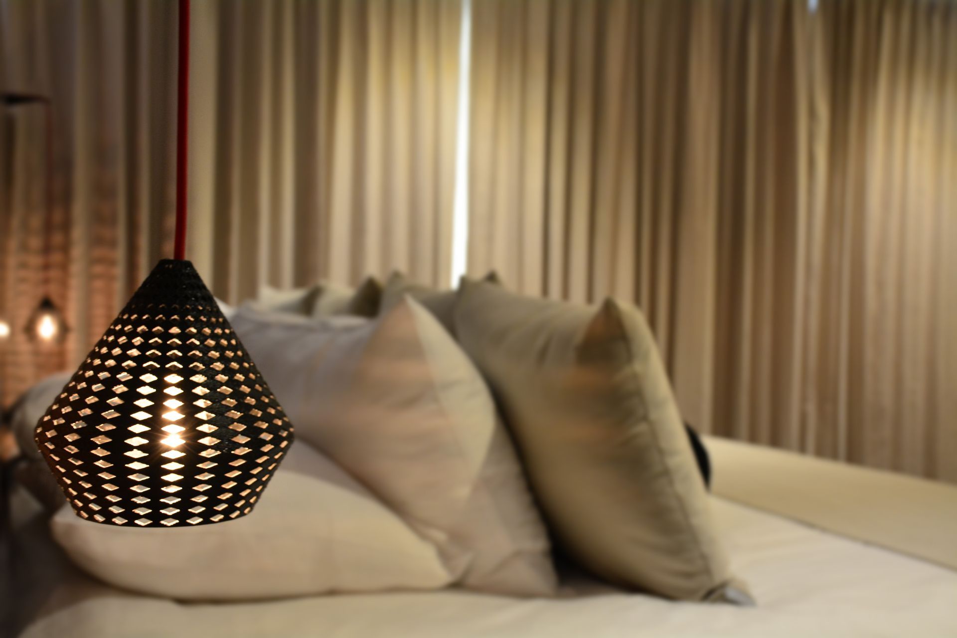 Lámpara colgante negra sobre una cama con almohadas y cortinas.