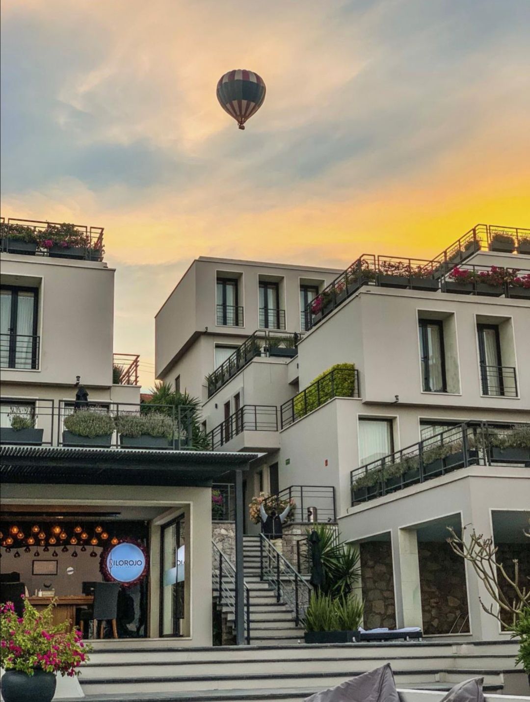 Globo aerostático sobre modernos edificios blancos con jardines en la azotea al atardecer.