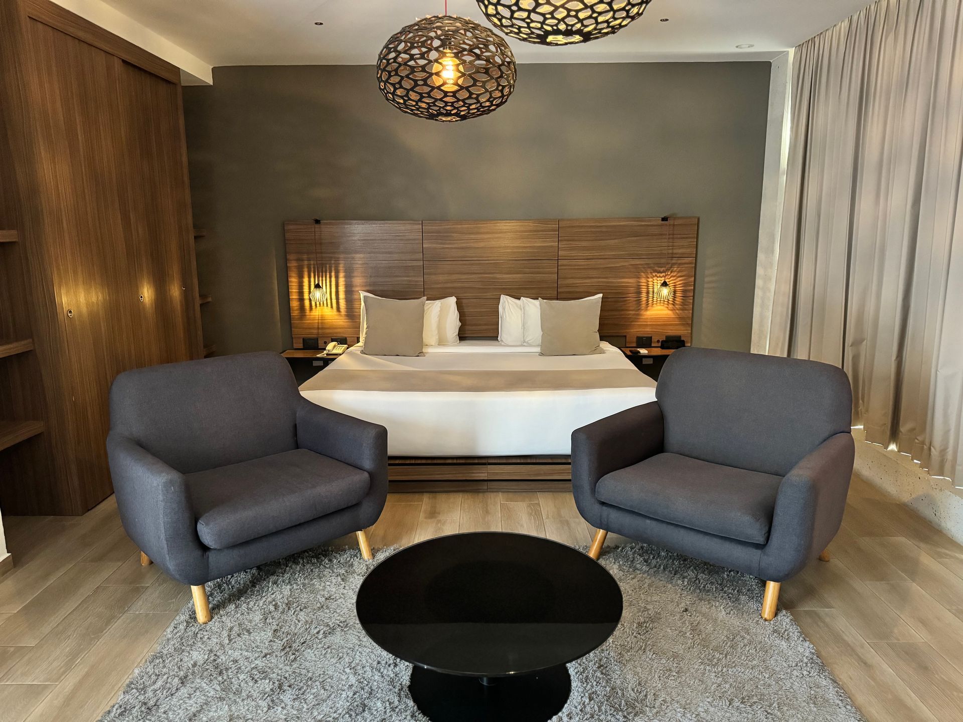 Dormitorio con cama king size, dos sillones, mesa redonda e iluminación decorativa.