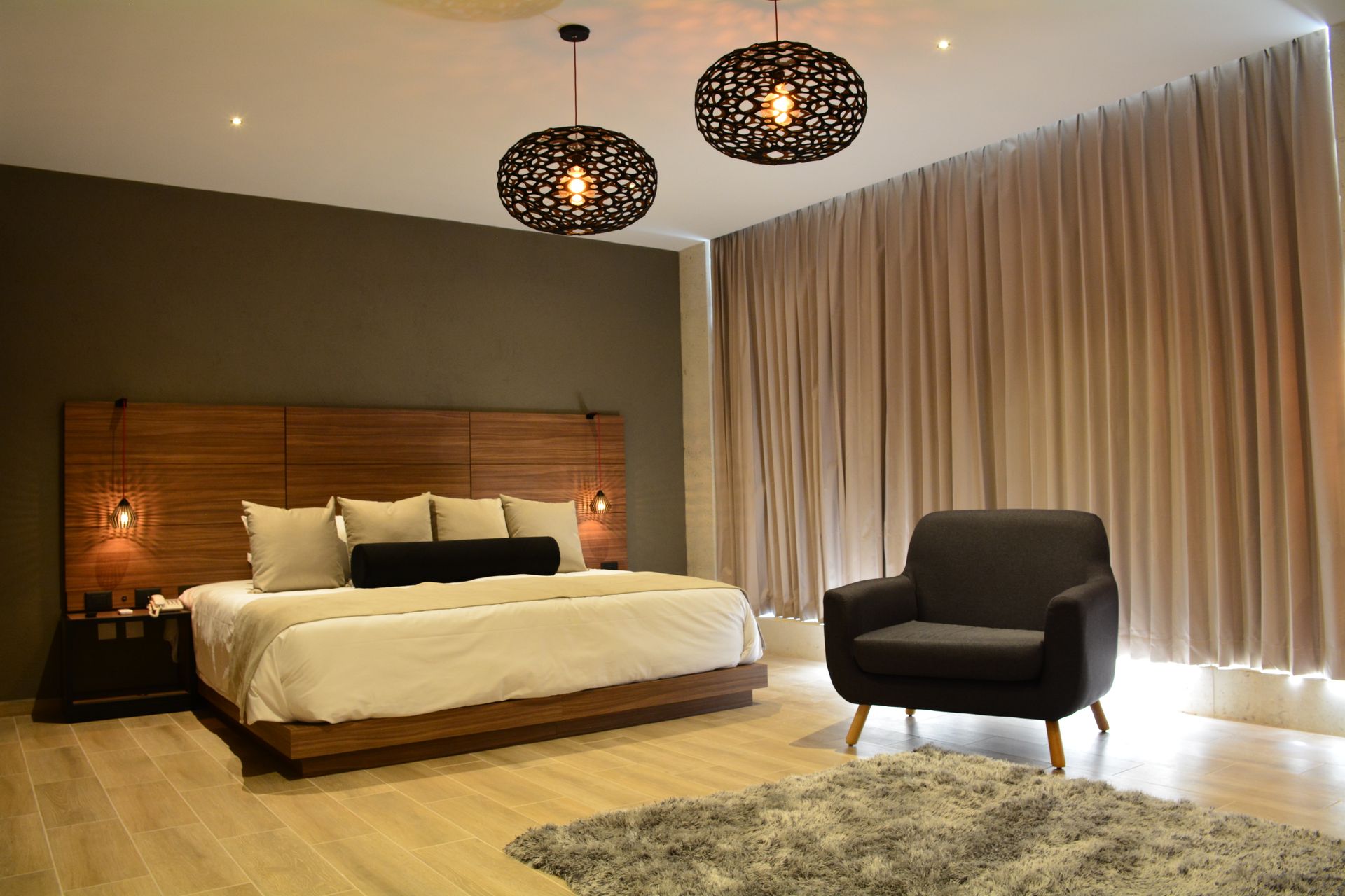 Dormitorio con cama, sillón, cortinas e iluminación decorativa.