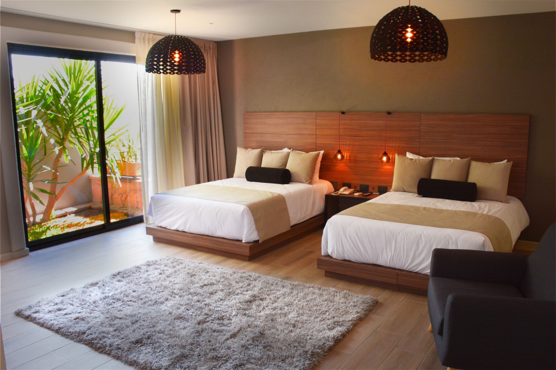 Habitación de hotel con dos camas, alfombra, puerta corrediza de vidrio e iluminación decorativa.