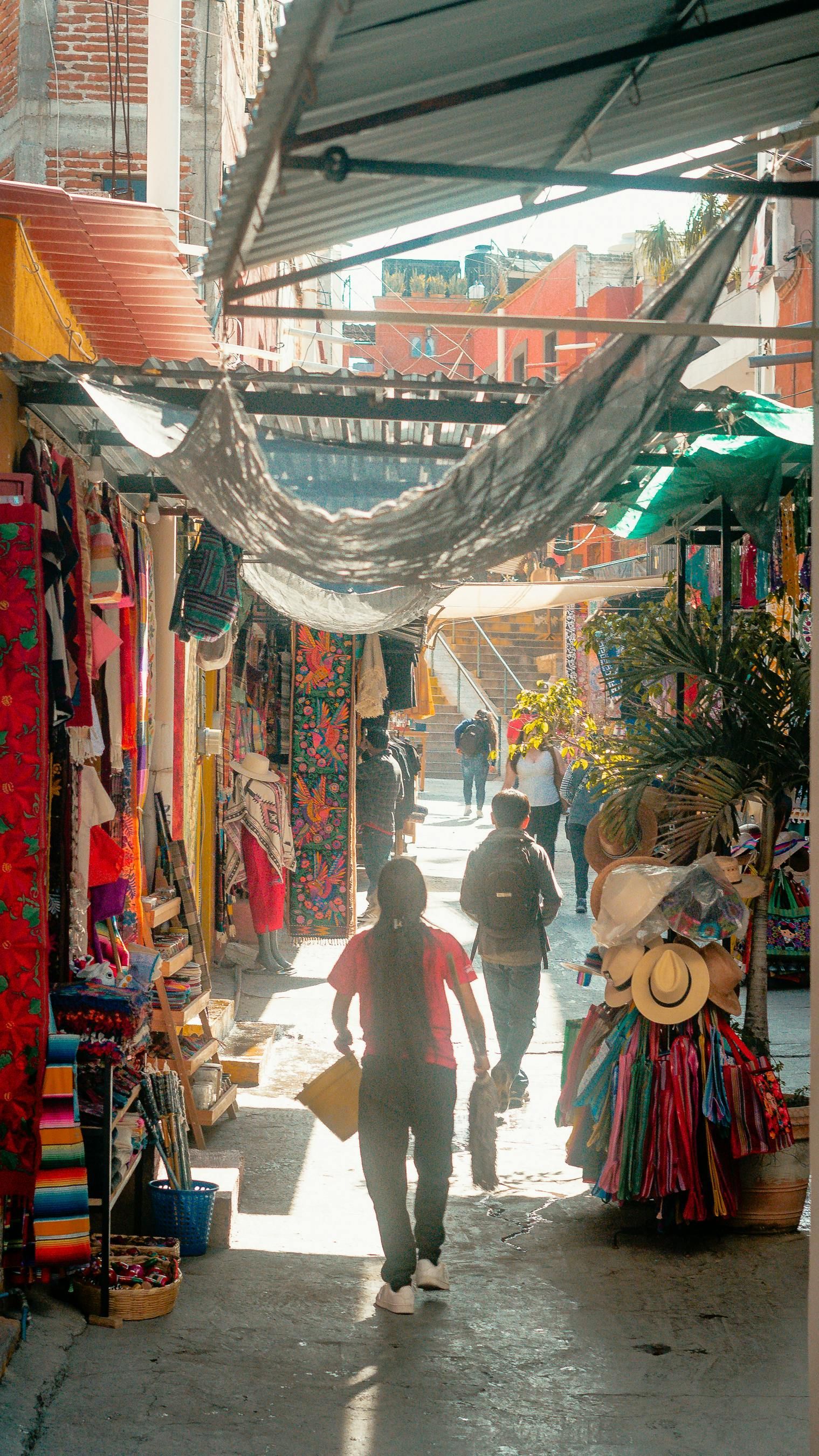 Una calle estrecha con mercado, llena de tiendas y vendedores. Gente paseando por el callejón bajo la luz del sol.