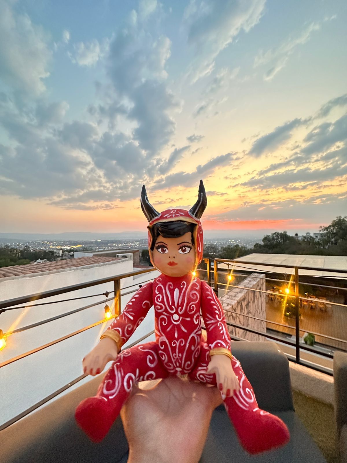 Una muñeca roja con cuernos se sienta en una mano contra un cielo al atardecer.