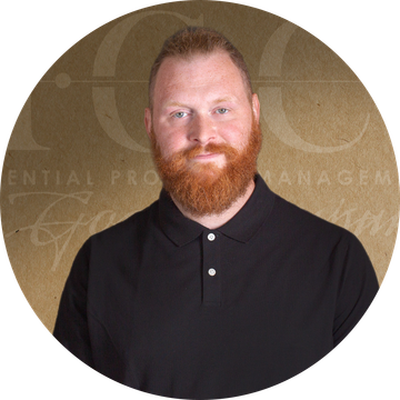 Man with ginger hair wearing a black collared shirt, against a brown background.