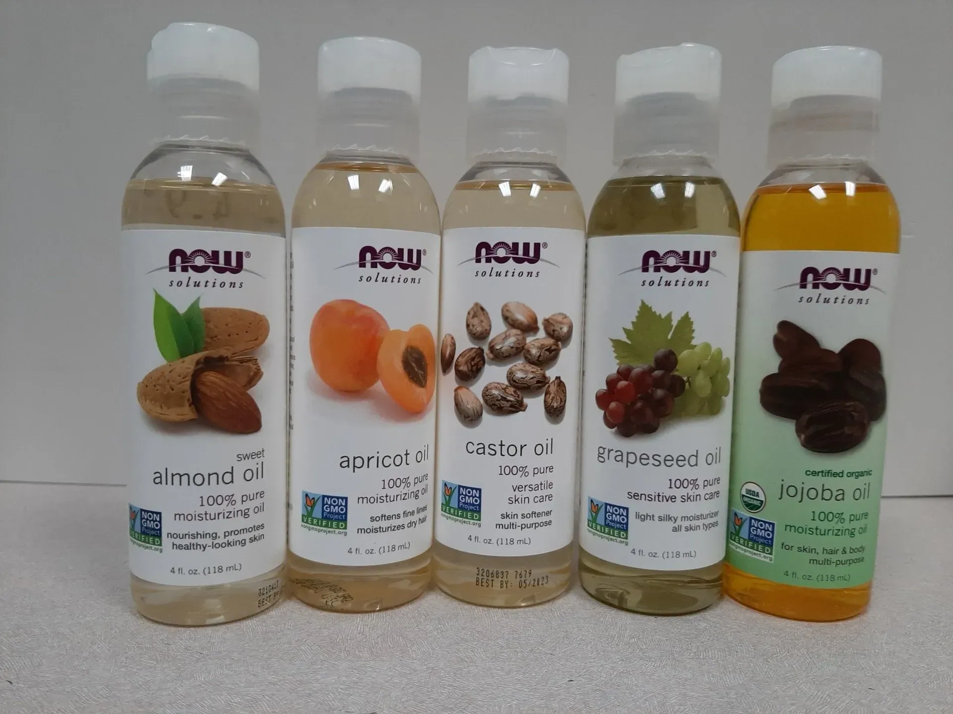 Five clear plastic bottles of NOW Solutions plant-based oils lined up in a row against a light background.