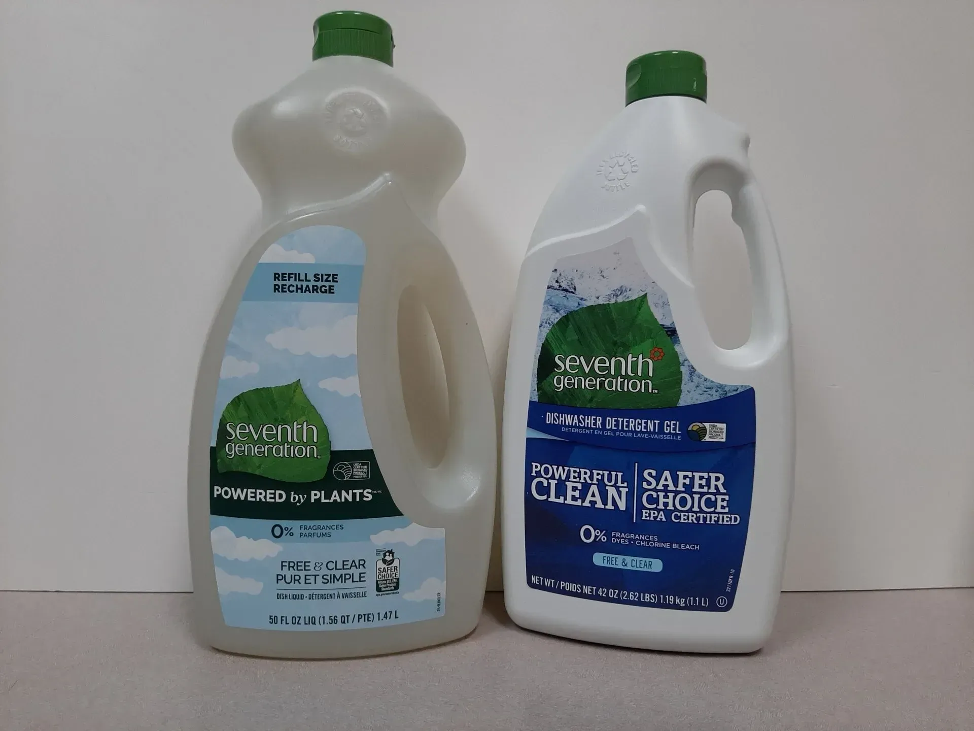 Two Seventh Generation liquid soap bottles, one clear and one opaque white, standing side-by-side on a light surface.