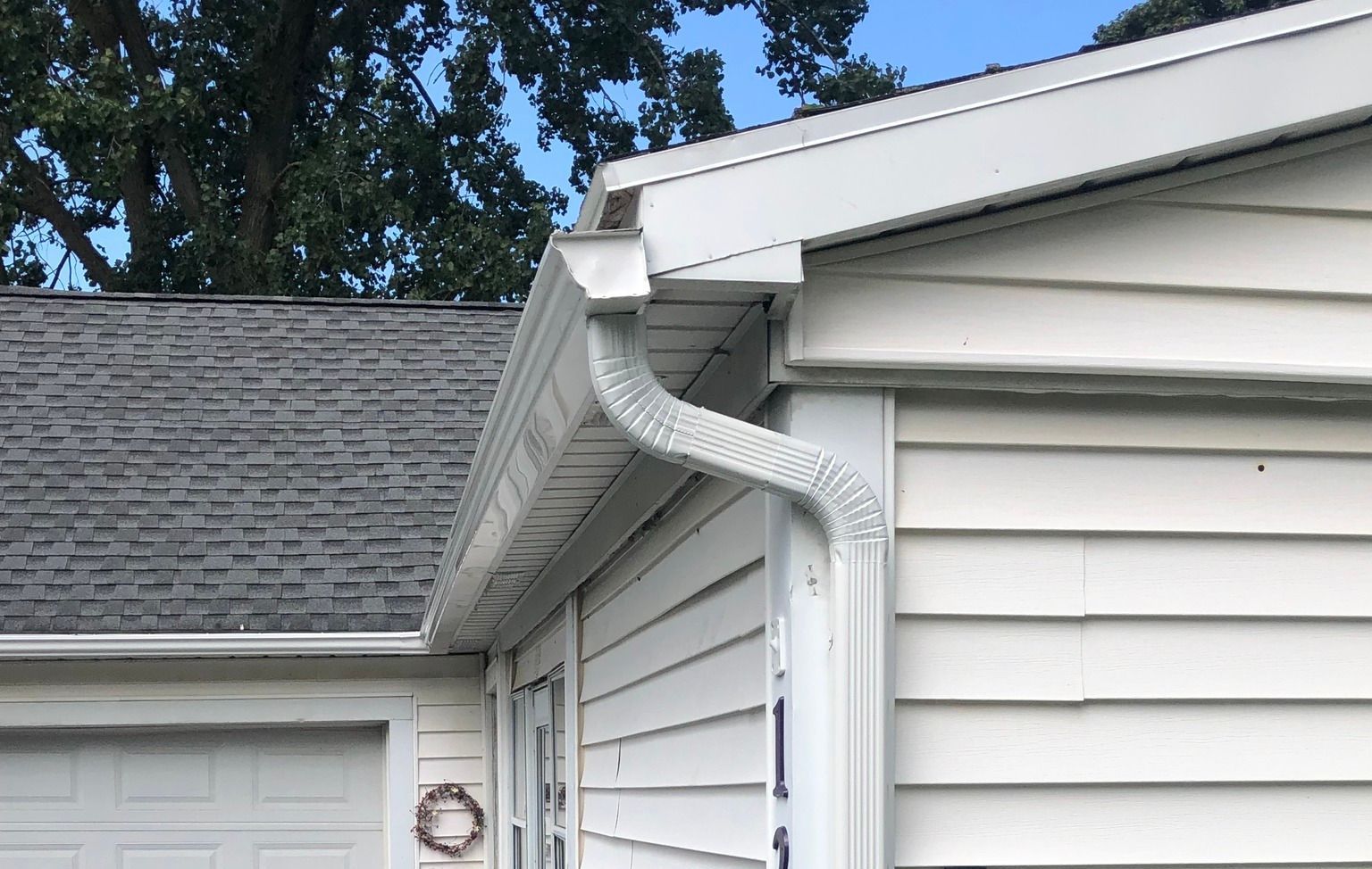 A new gutter system, installed on a white house, seen from below the spout on the corner.