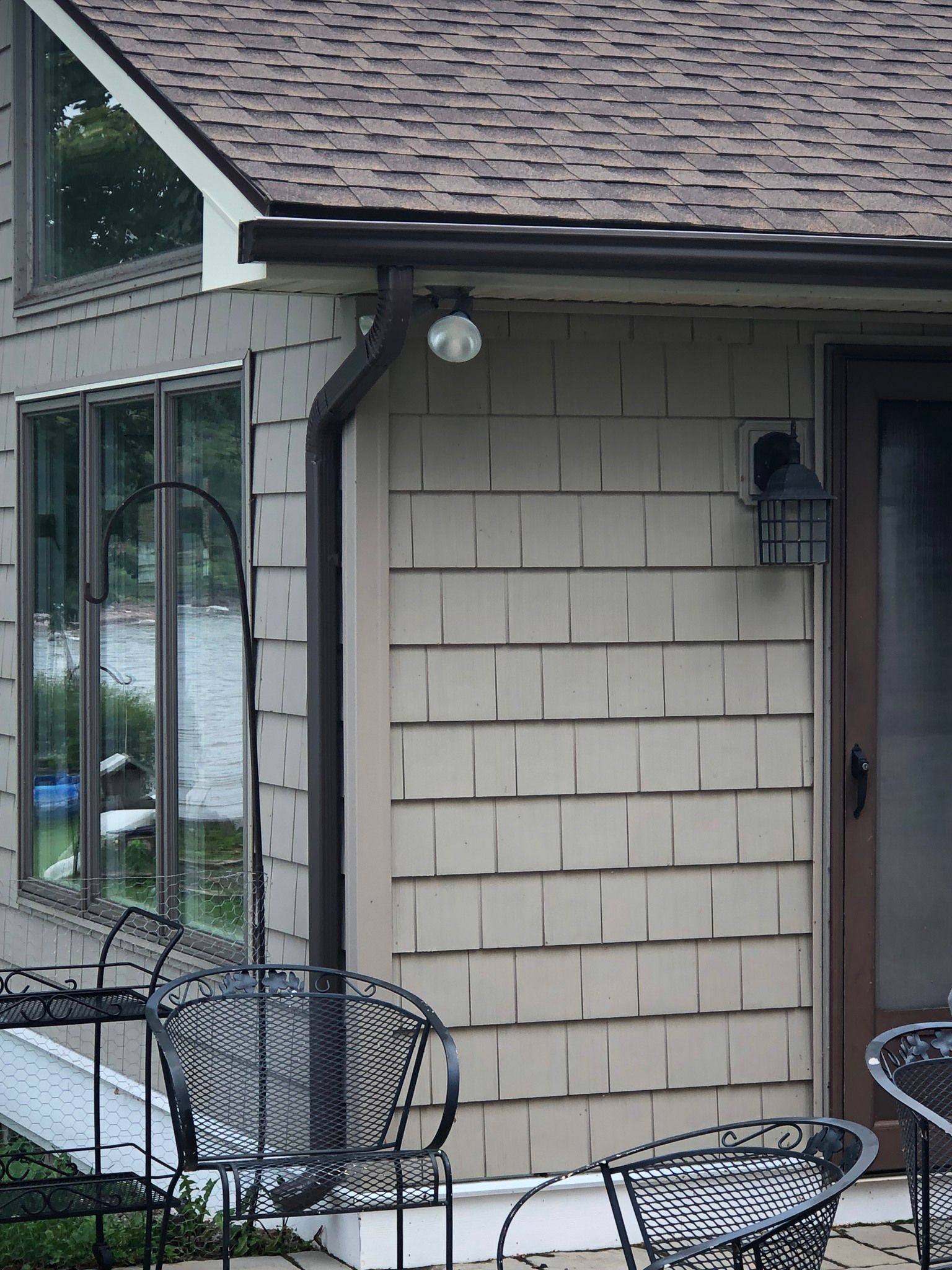 A new black gutter spout installed in a nice cream-colored house.
