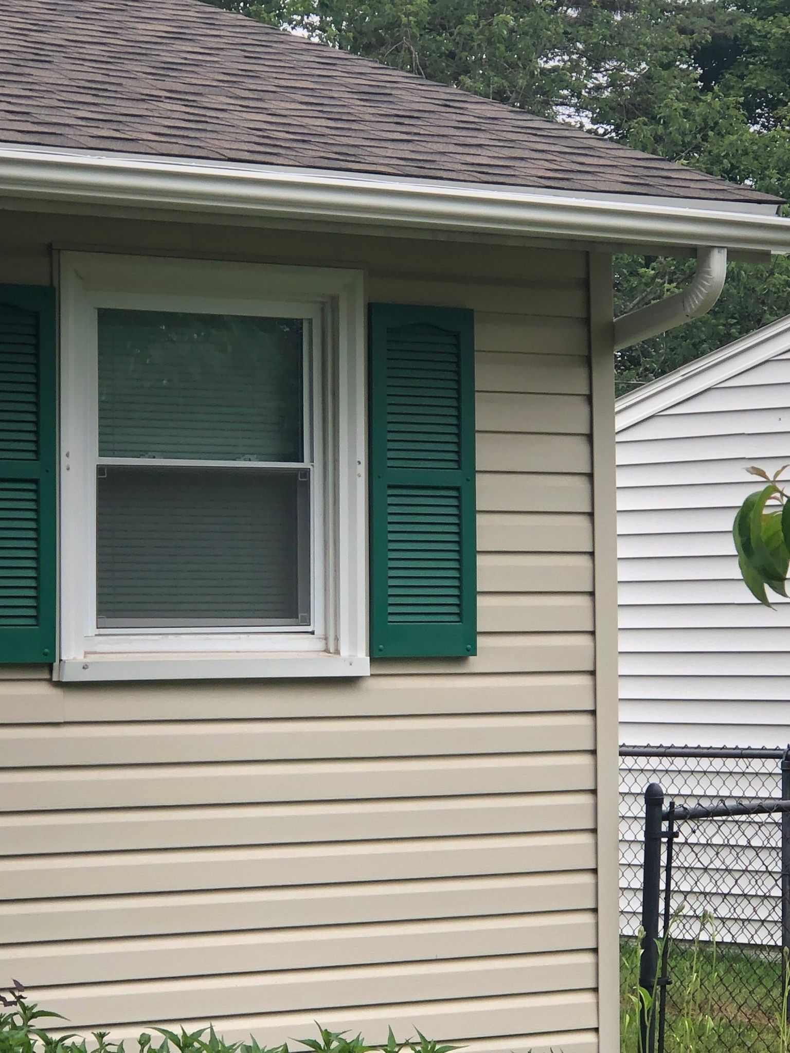 House with green shutters and tan siding after a gutter replacement