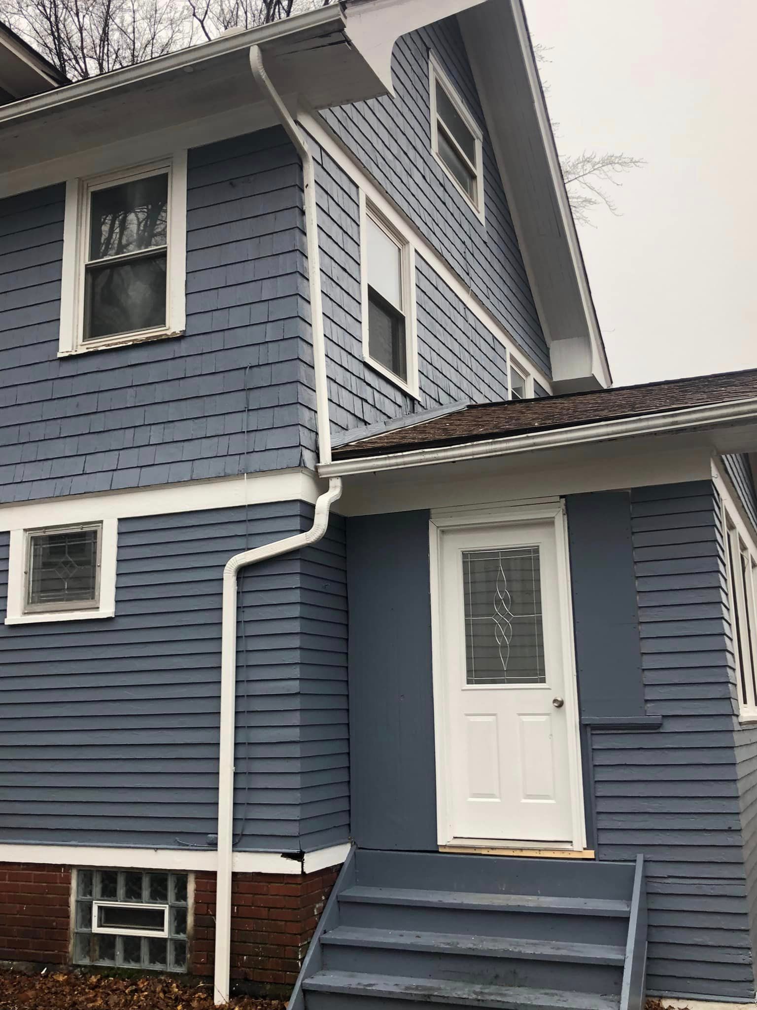 Two story downspout and gutters after replacement done on a dark blue house