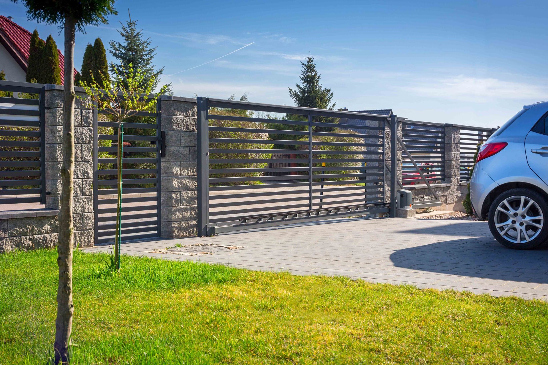 Wooden slat fence beside a driveway, with grass in front and a blue car parked at right.