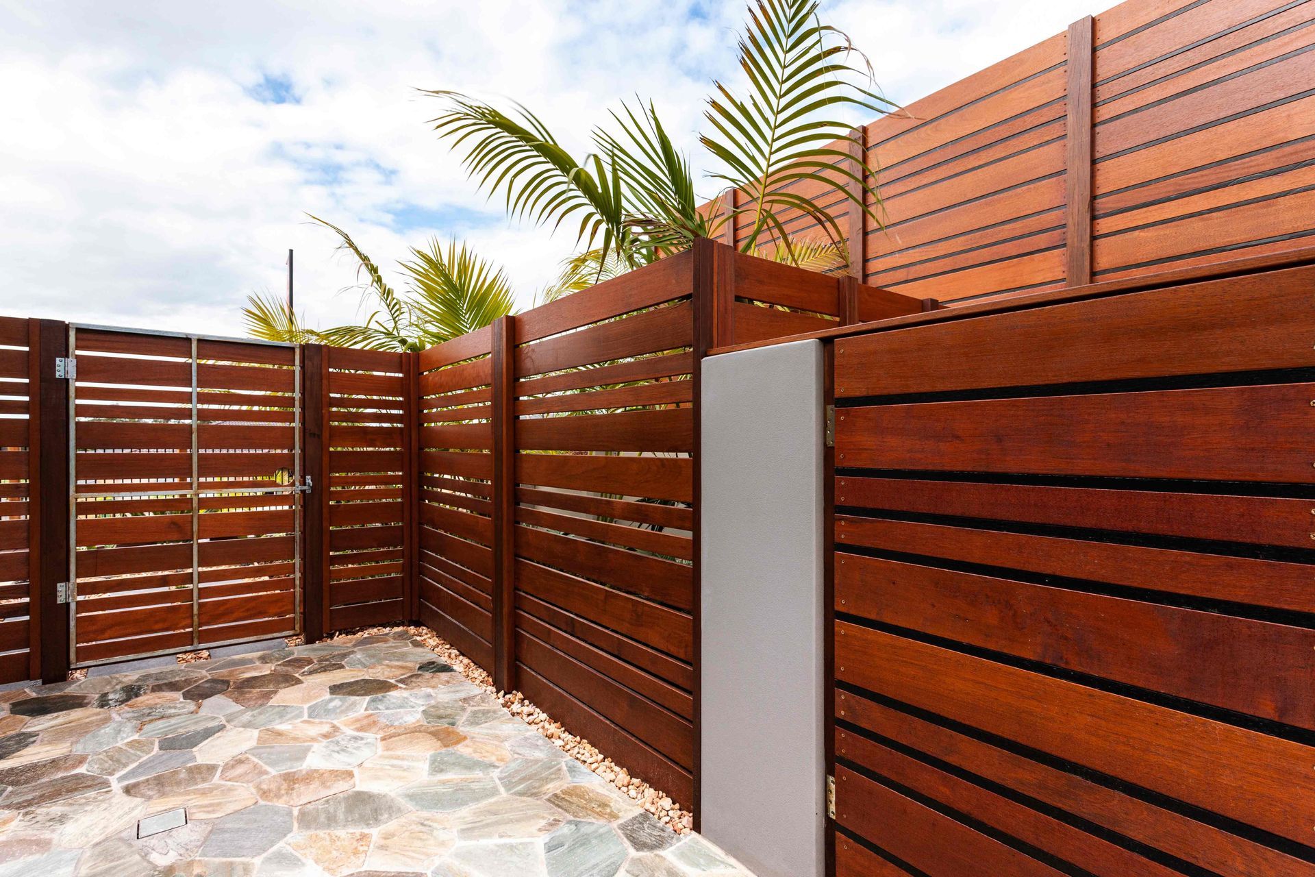 Modern backyard with horizontal wood privacy fence, stone patio, and palm plants Modern backyard with horizontal wood privacy fence, stone patio, and palm plants